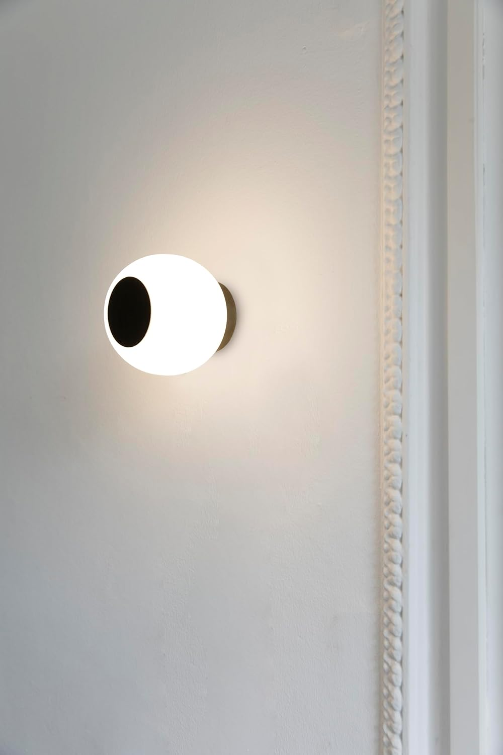 Una moderna applique da parete con forma ovale bianca e un ritaglio circolare nero, montata su un muro bianco.