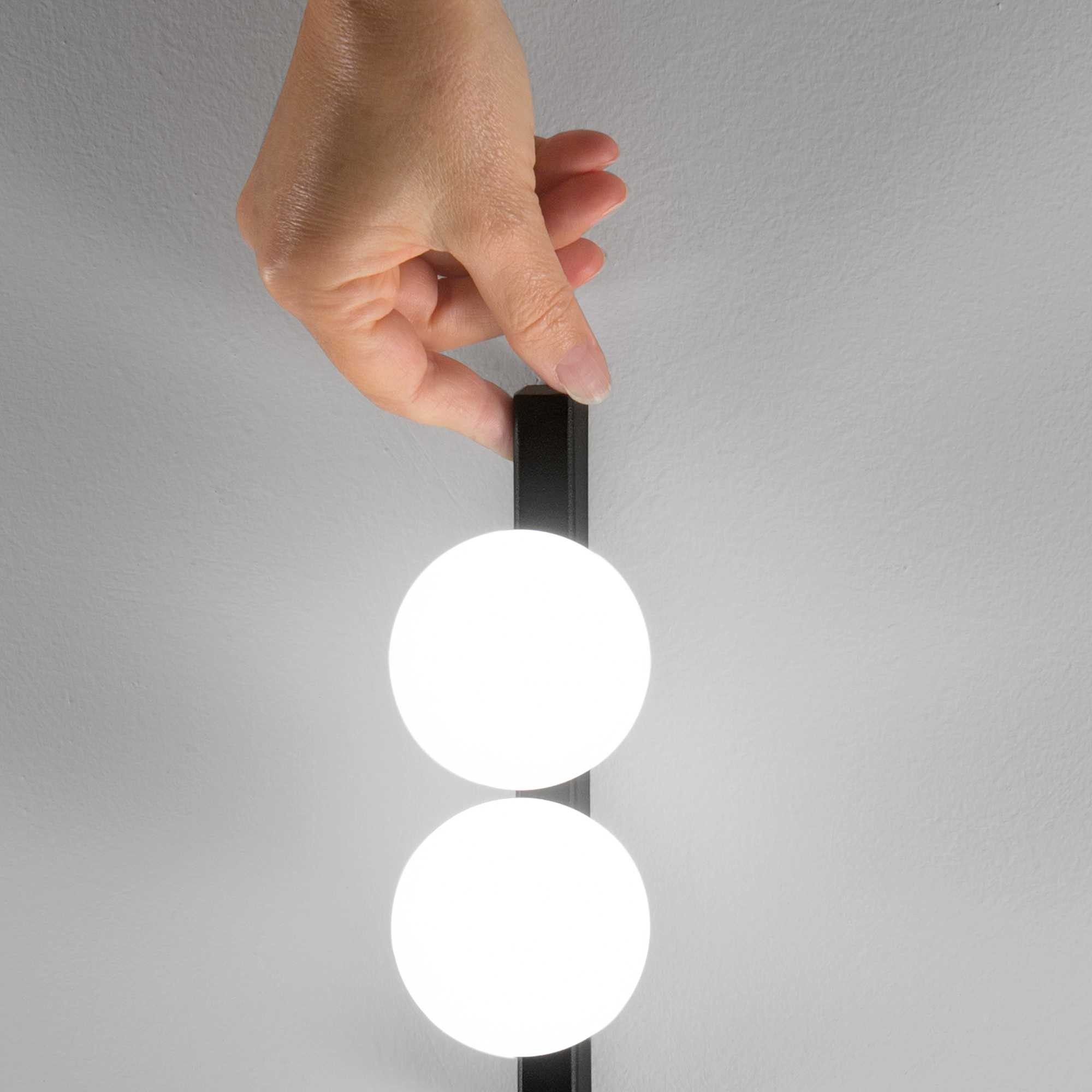 Una mano tiene un accessorio nero con due luci circolari bianche luminose contro un muro grigio.