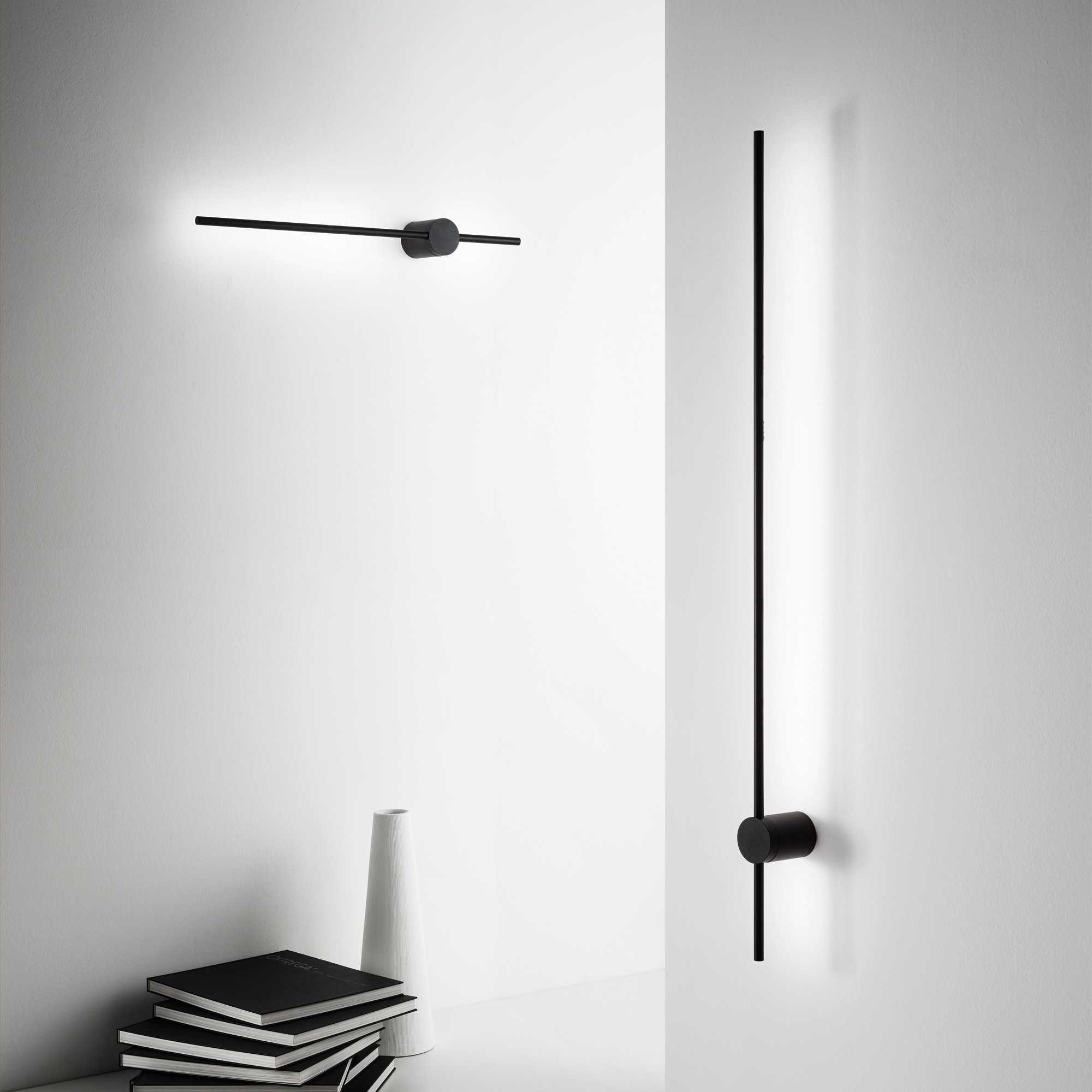 Un muro bianco con due lampade nere moderne e libri. Una lampada è verticale, l'altra è orizzontale.