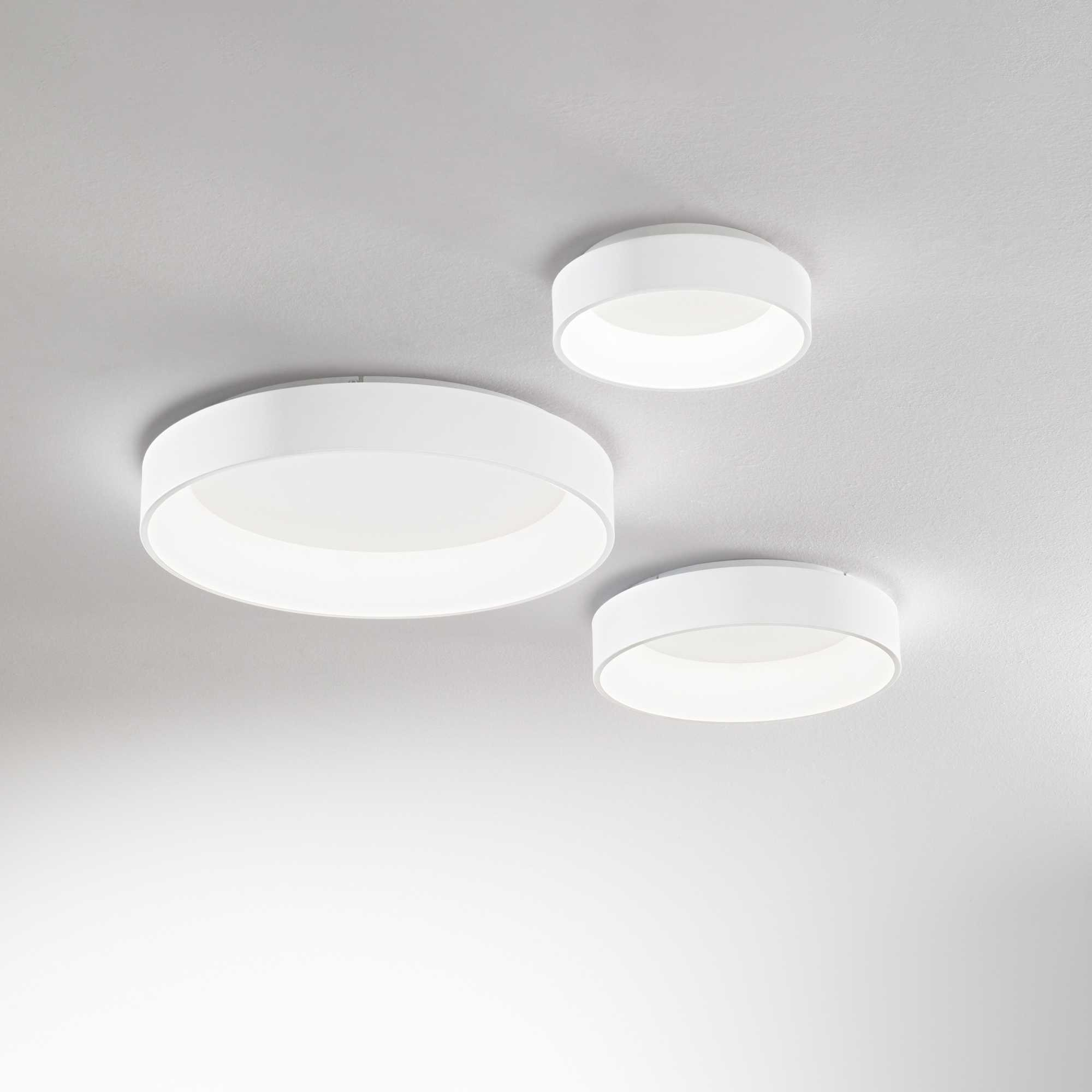 Tre lampade da soffitto circolari bianche, di dimensioni variabili, montate su un soffitto bianco.