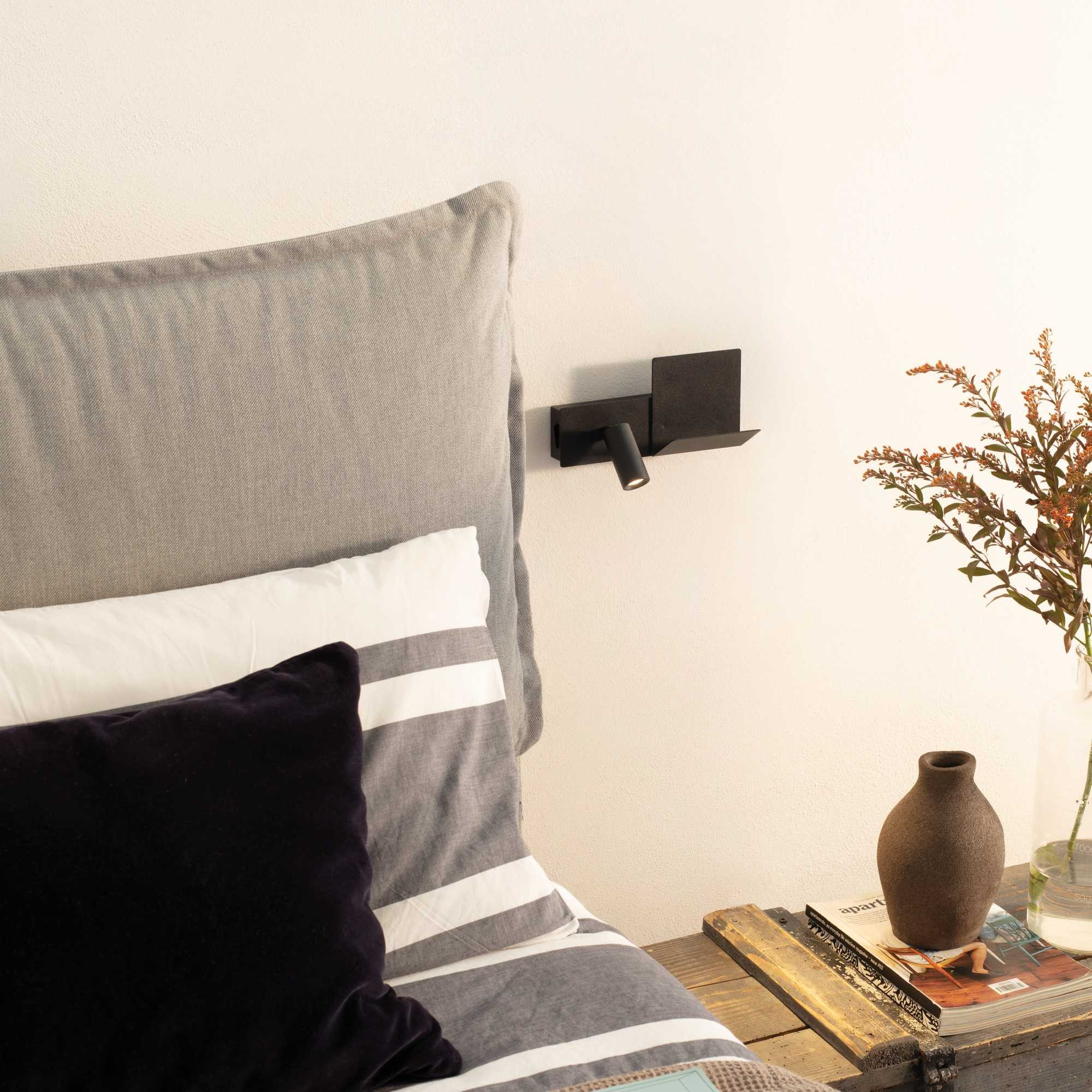 Scena della camera da letto. Letto con cuscini, lampada, vaso con fiori e rivista su tavolo legno.