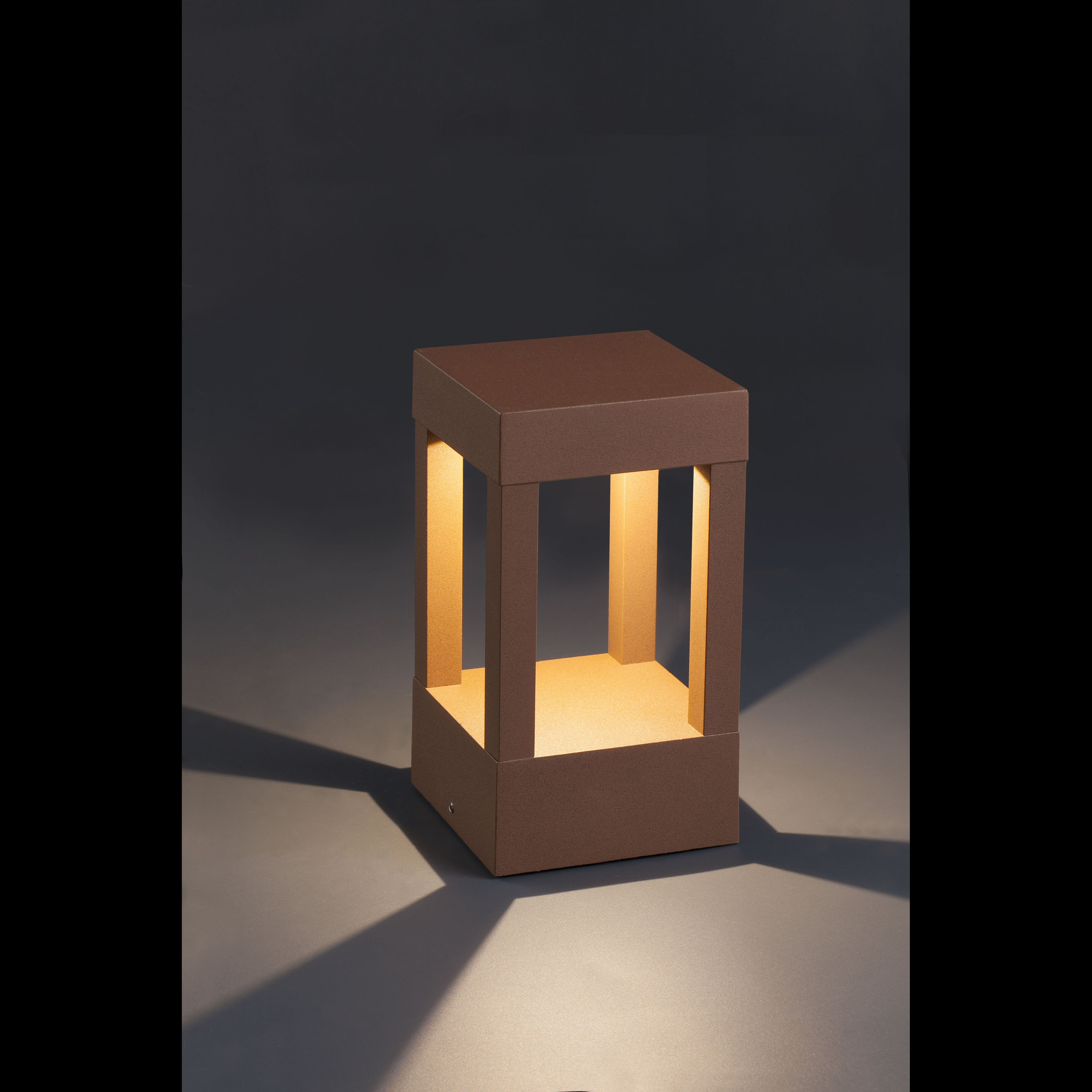Una lampada quadrata marrone con interno illuminato si trova su una superficie grigia. Ombre su sfondo grigio.