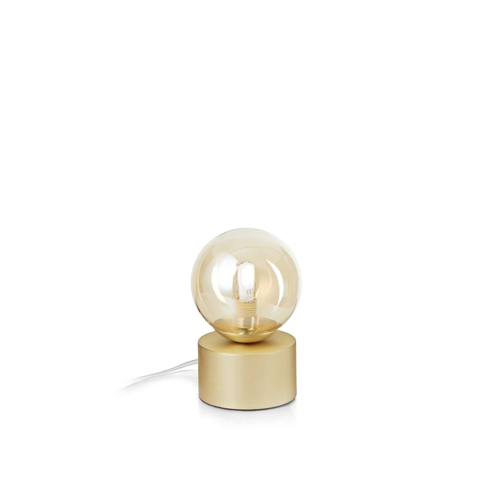 Lampada da tavolo dorata con paralume rotondo in vetro ambrato su base cilindrica. Un cavo bianco parte dalla base.