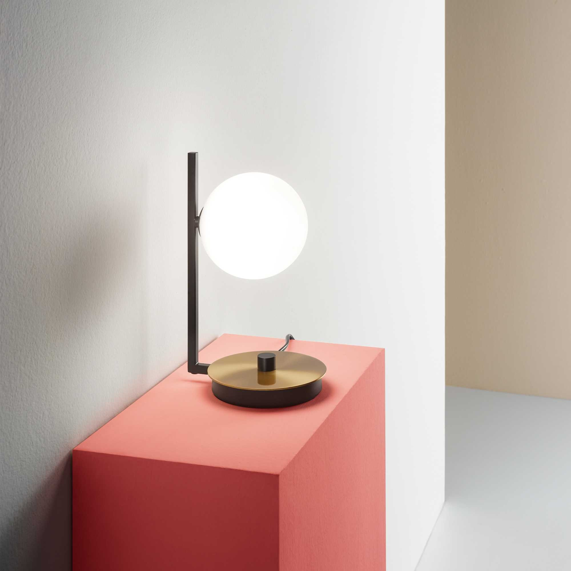 Una lampada moderna con luce sferica su un cubo rosa, contro pareti bianche e beige.