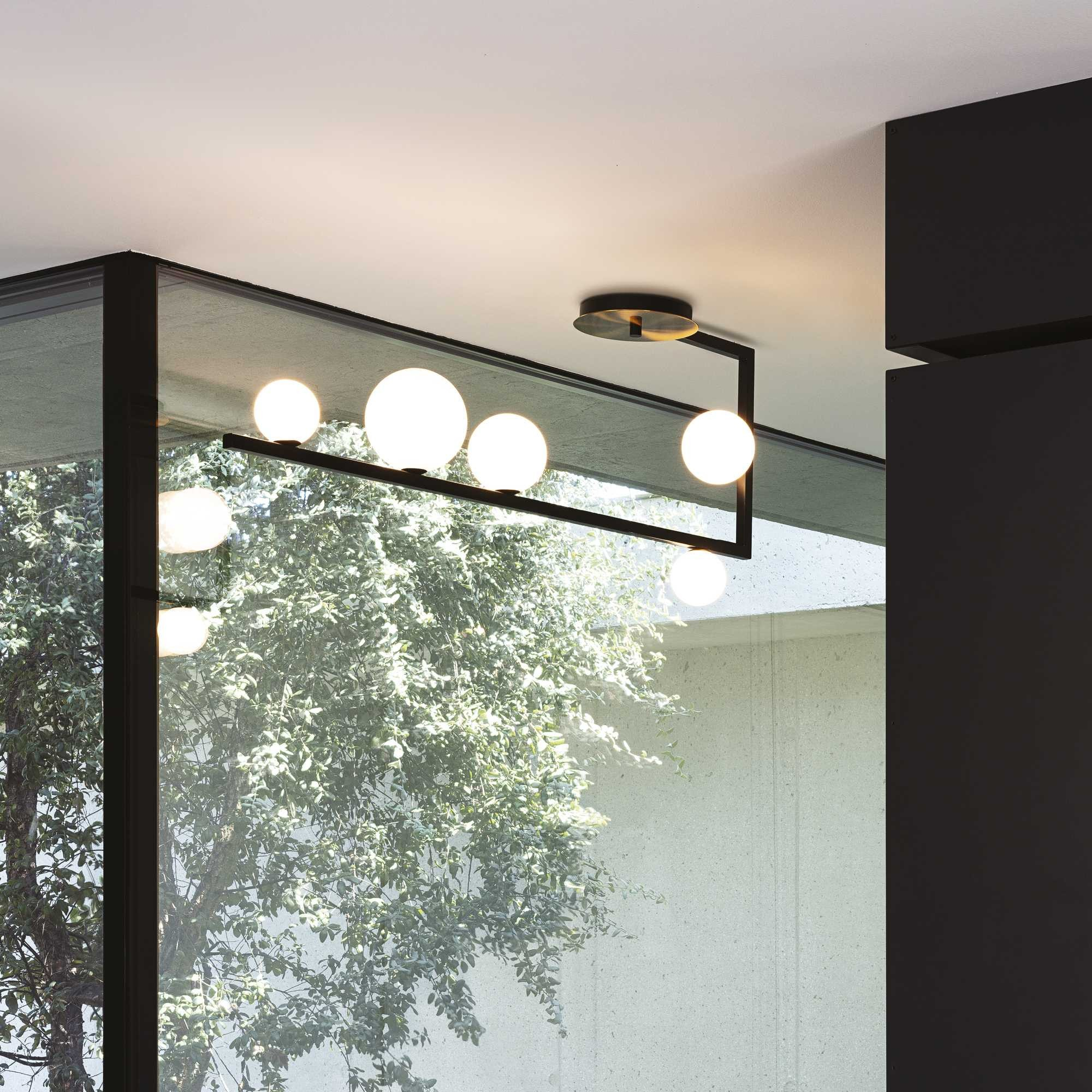 Un moderno apparecchio di illuminazione con lampadine sferiche, posto di fronte a una finestra con vegetazione verde.