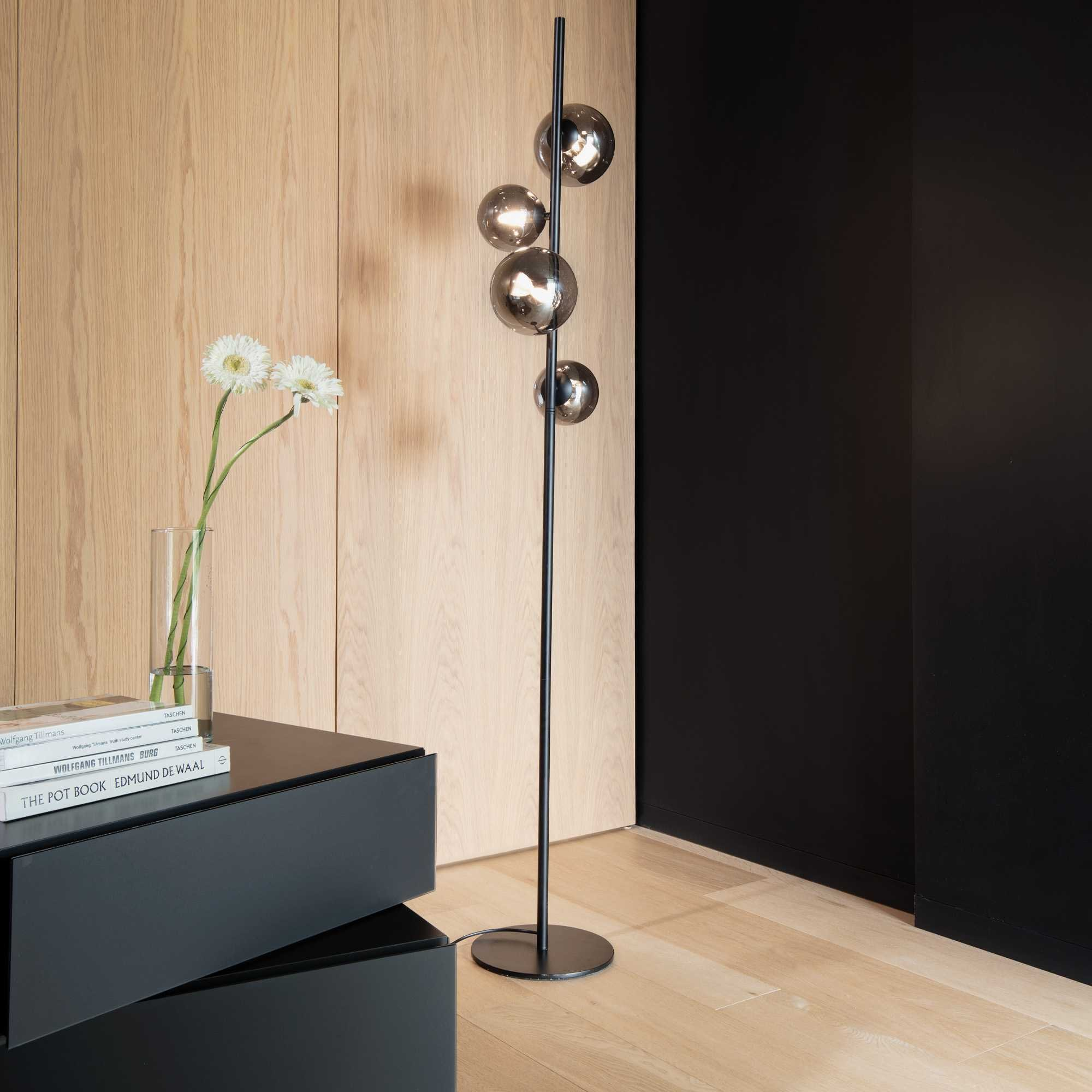 Una stanza moderna con una lampada da terra con luci sferiche, fiori in un vaso e un tavolino nero.