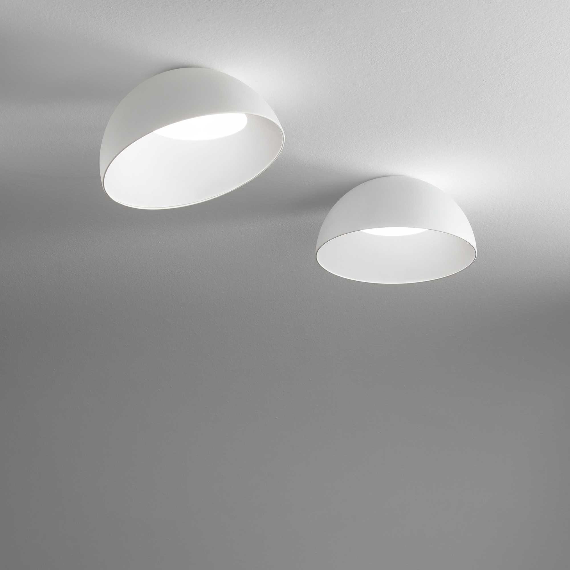 Due luci a soffitto bianche a forma di cupola contro soffitto bianco e parete grigia.