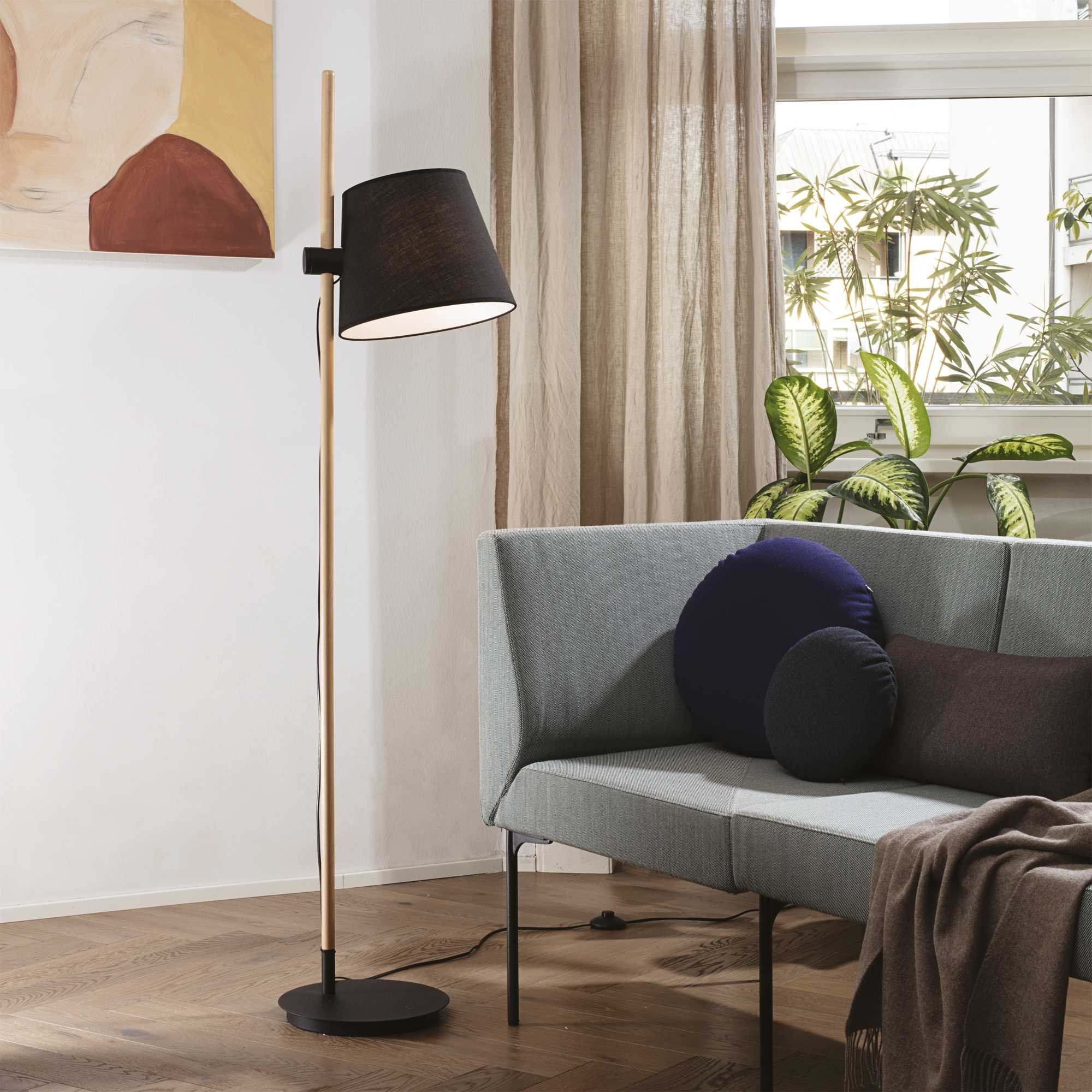 Un moderno soggiorno con una lampada da terra, un divano grigio con cuscini e una coperta e una finestra con tende.