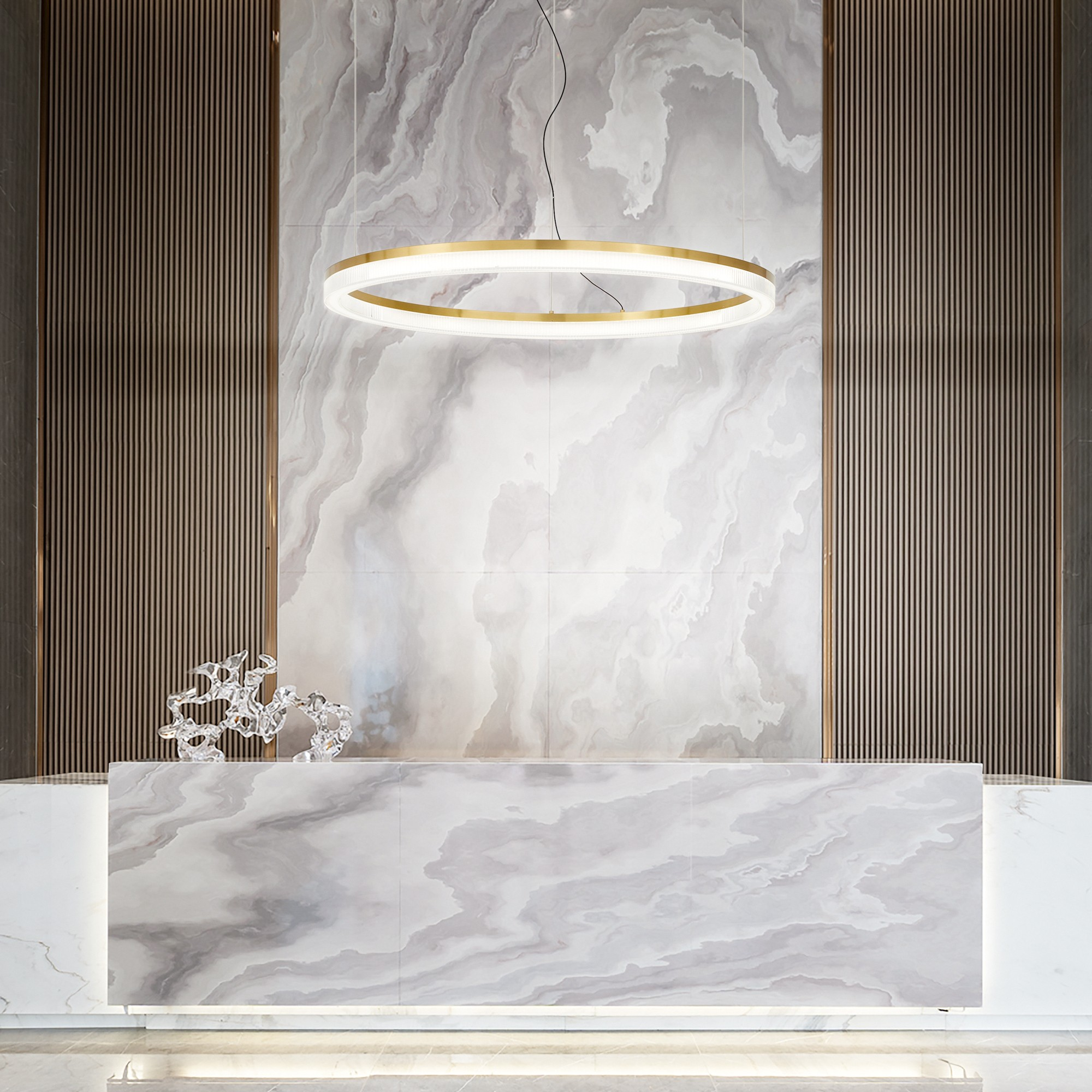 Un banco reception illuminato con piano in marmo. Sopra è appesa una grande luce circolare. Pannelli di legno sulla parete.