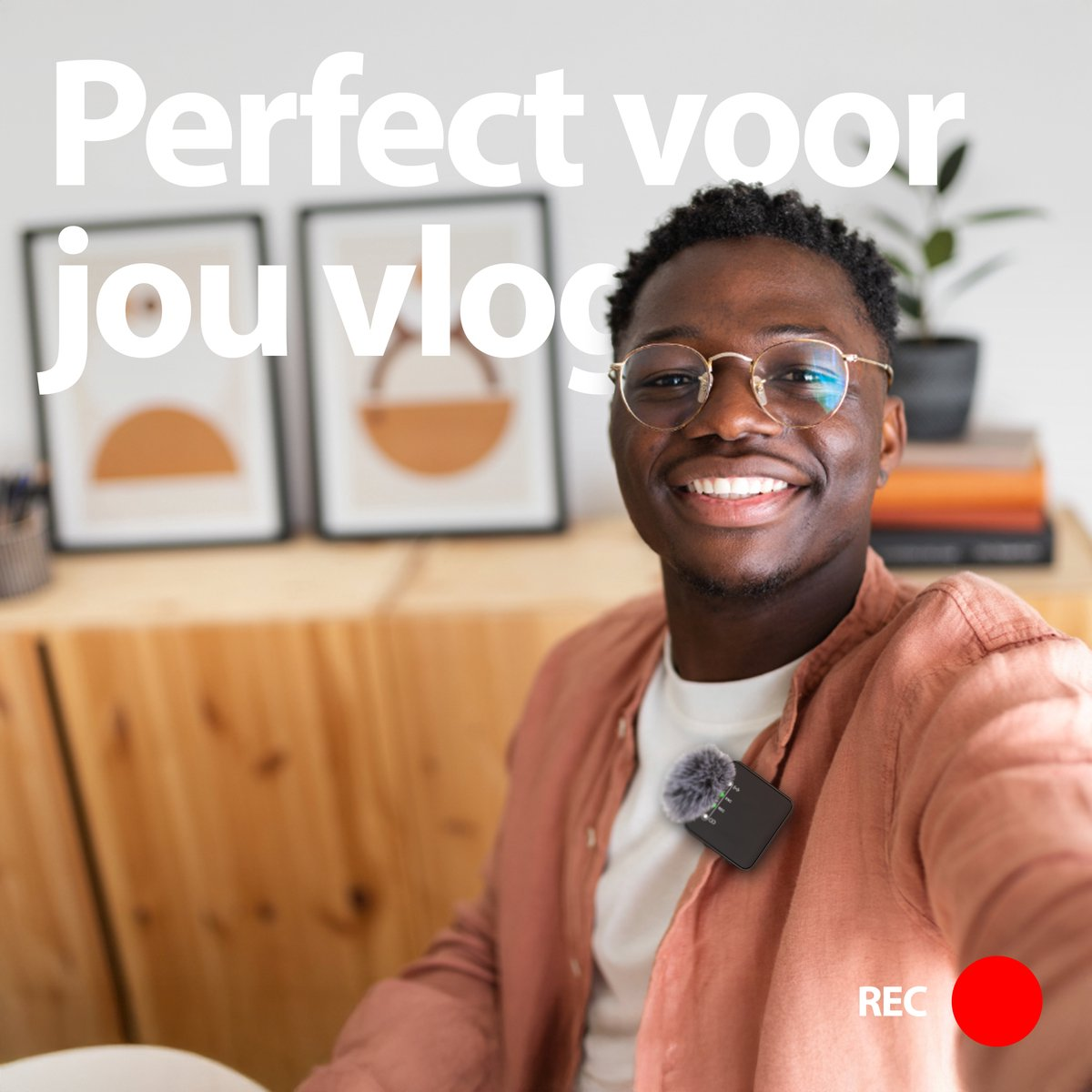 A smiling Black man with glasses takes a selfie. He wears a pink shirt and a lavalier microphone. Text reads 'Perfect voor jou vlog'.