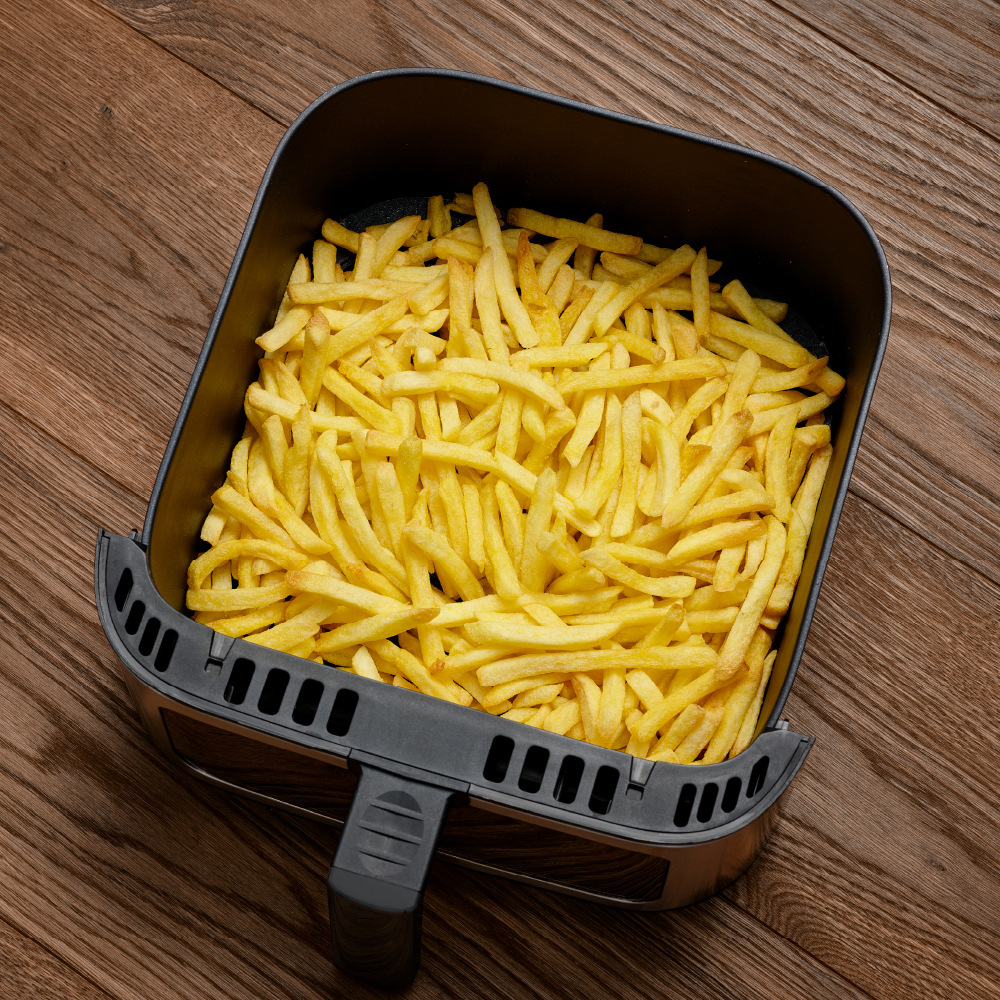Ein mit goldbraunen Pommes gefüllter Frittierkorb steht auf einem Holztisch. Der Frittierer ist schwarz und silber.