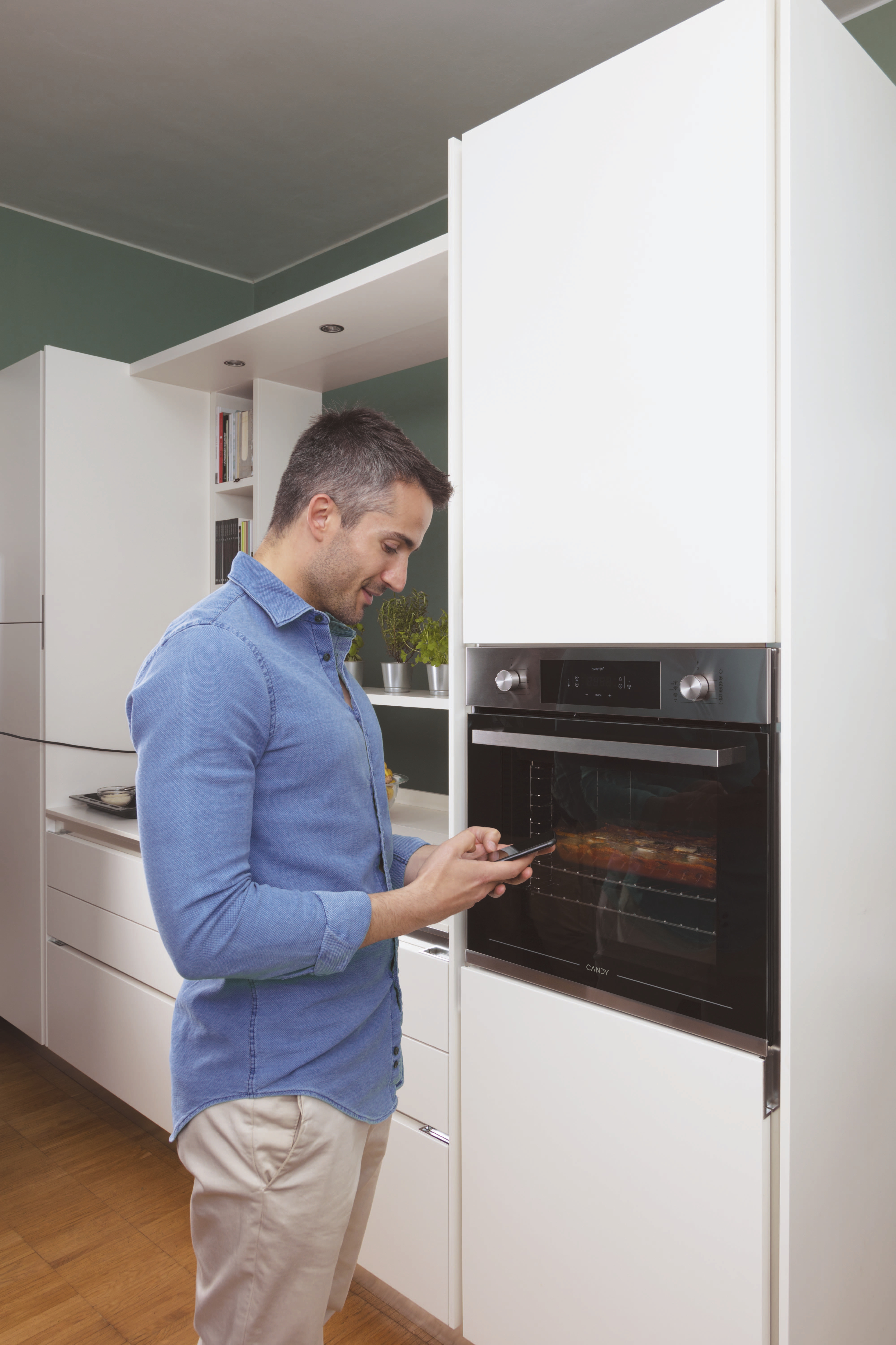 Un uomo con una camicia blu usa il telefono in una cucina moderna. Un forno è acceso.