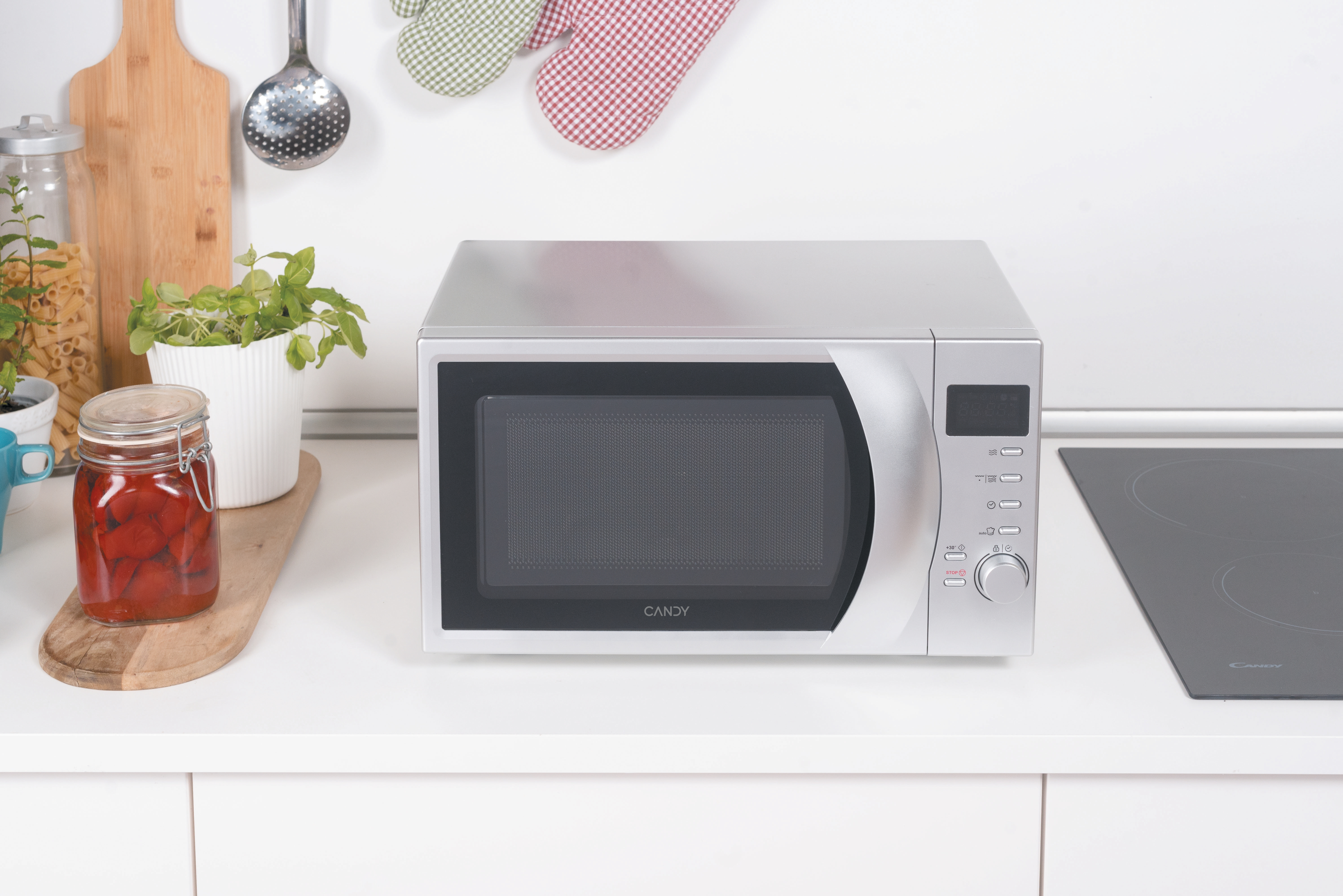 Un forno a microonde è appoggiato su un piano della cucina. Sono presenti anche barattoli, piante e utensili da cucina.