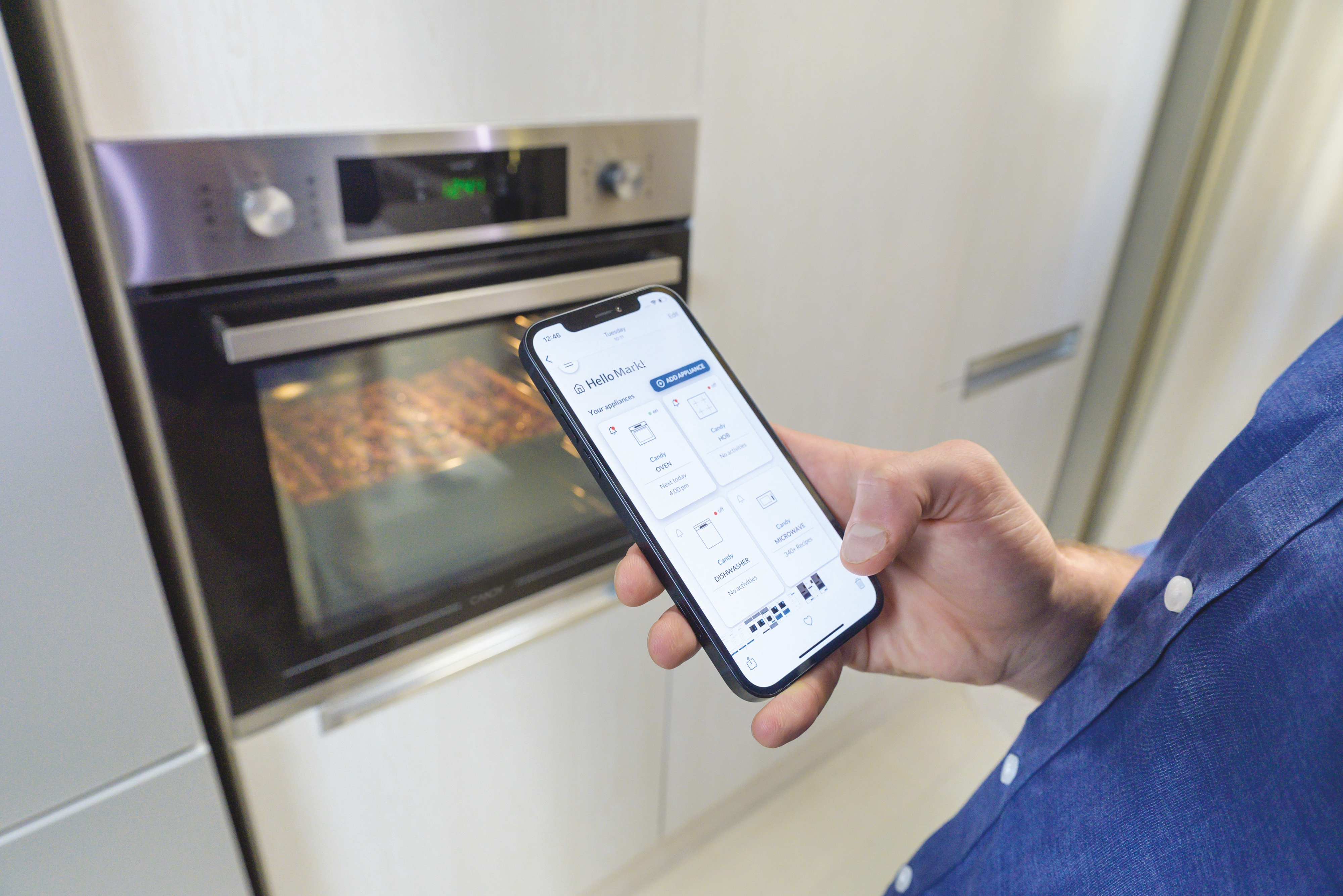 Una persona tiene in mano un telefono che mostra i comandi del forno davanti a un forno a incasso in cucina.