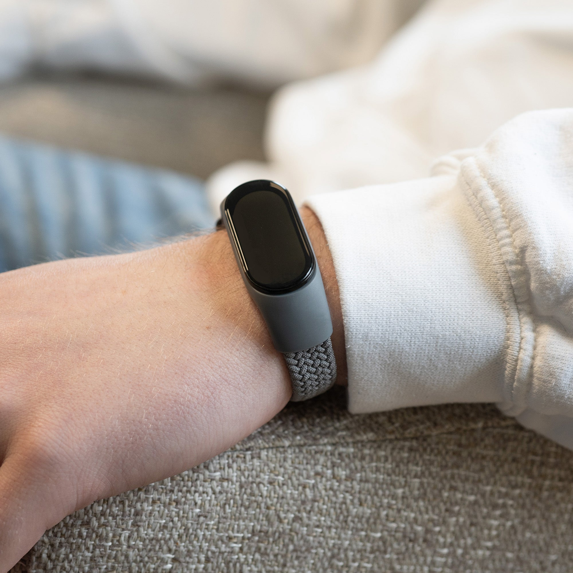 Das Handgelenk einer Person mit einer grauen Smartwatch. Die Person trägt einen weißen Pullover.