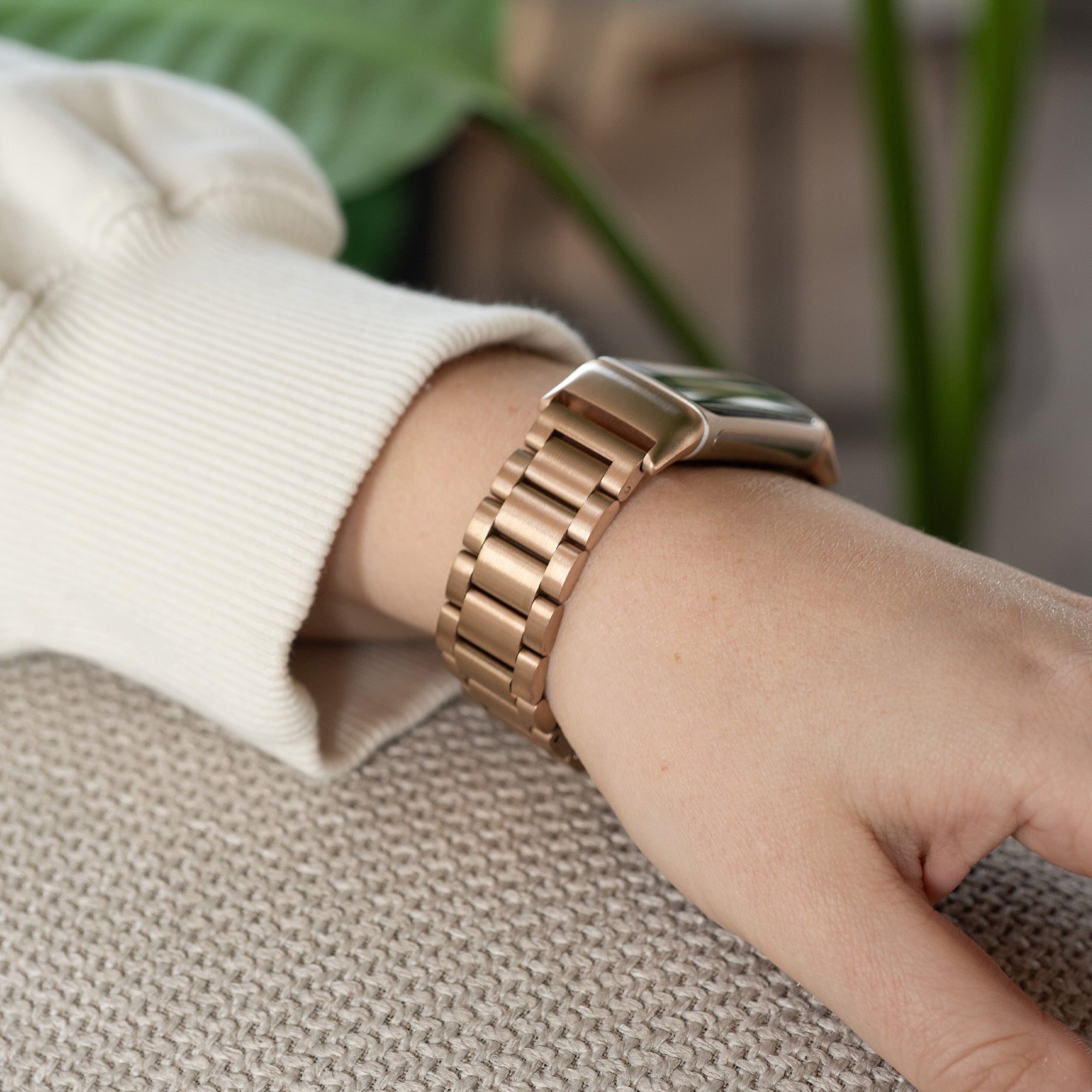 Das Handgelenk einer Person mit einer roségoldenen Uhr. Der Arm ruht auf einer strukturierten Oberfläche, verschwommener Hintergrund.