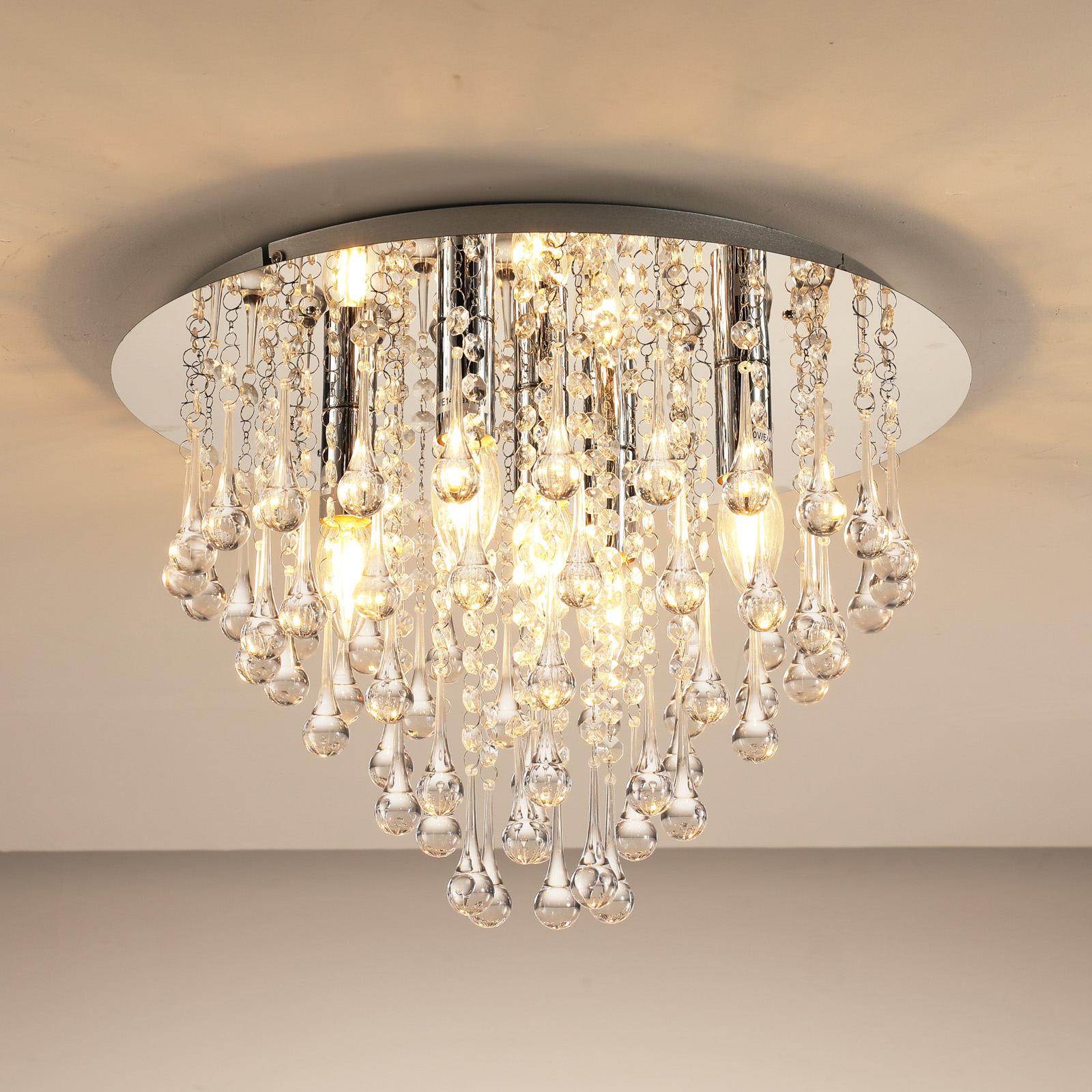 Ein Kronleuchter aus Kristall hängt von der Decke. Er hat viele tropfenförmige Kristalle und mehrere Lichter sind an.