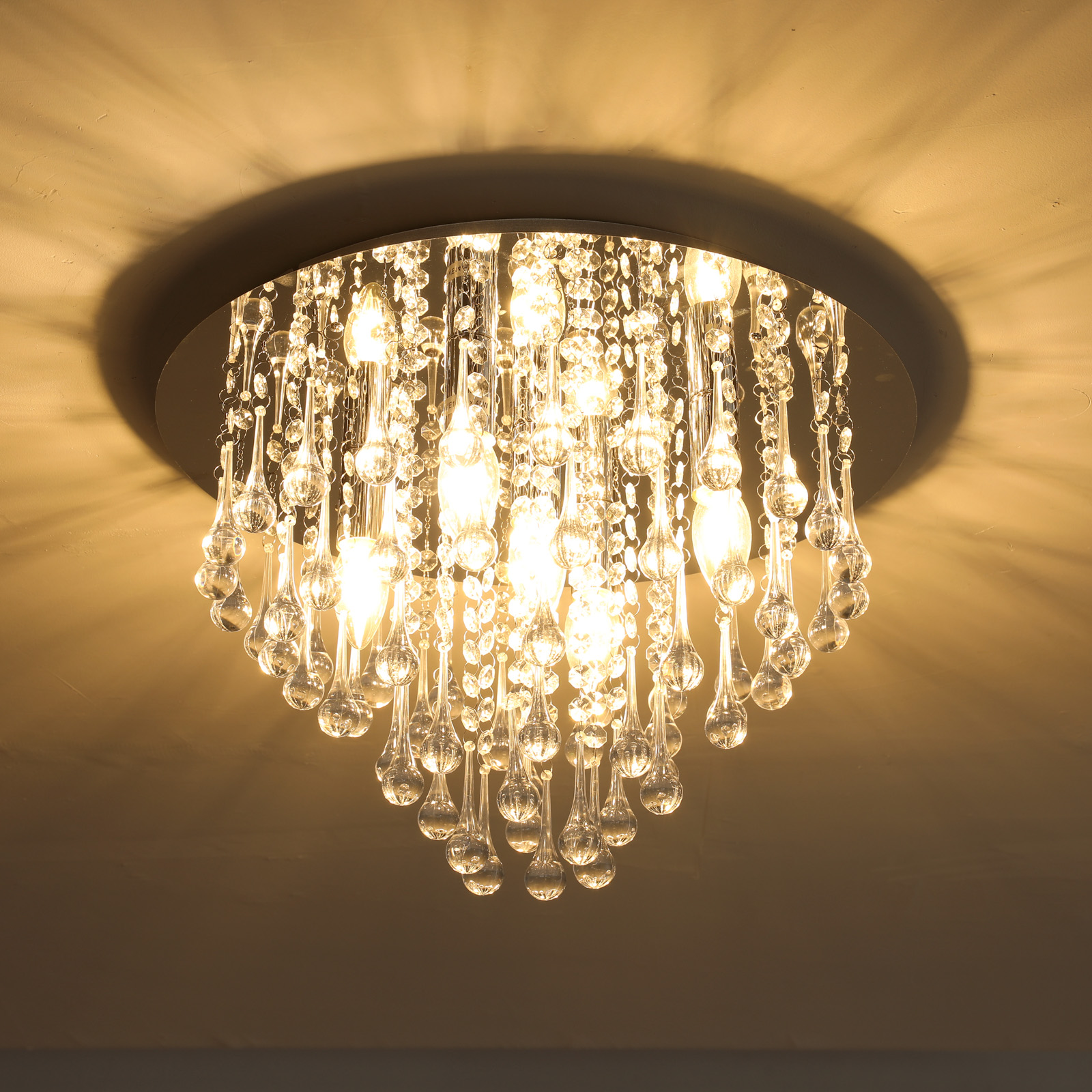 Ein Kronleuchter hängt an der Decke. Er hat viele klare, tropfenförmige Kristalle und Lichter.
