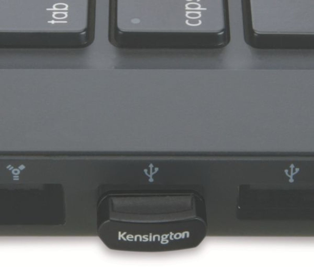 Primo piano dell'hub USB e della tastiera di un laptop nero. Visibile una porta USB Kensington nera. La tastiera ha tasti 'tab' e 'caps'.