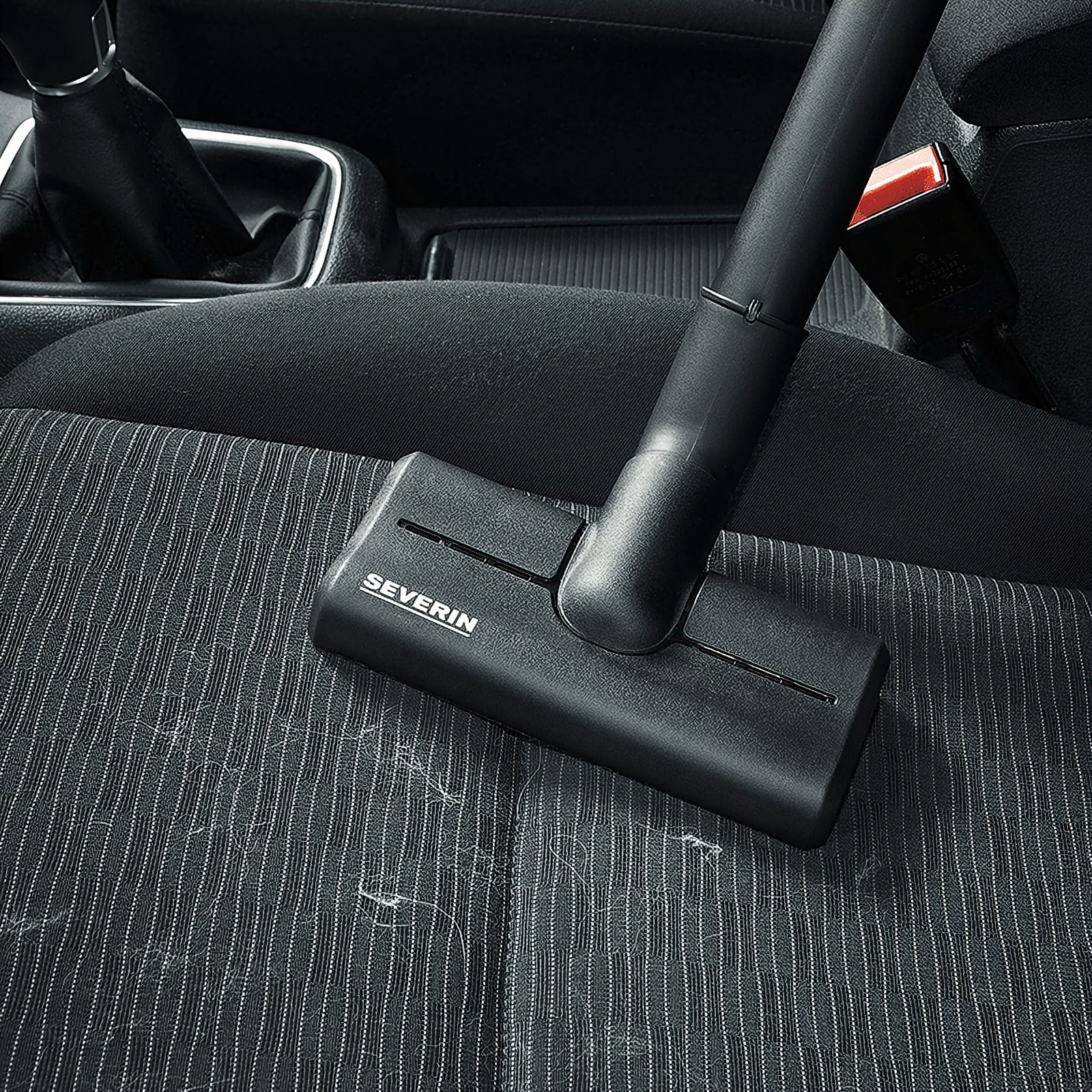 Czarny odkurzacz czyści siedzenie samochodu. Siedzenie jest czarne z białymi paskami i ma włosy.