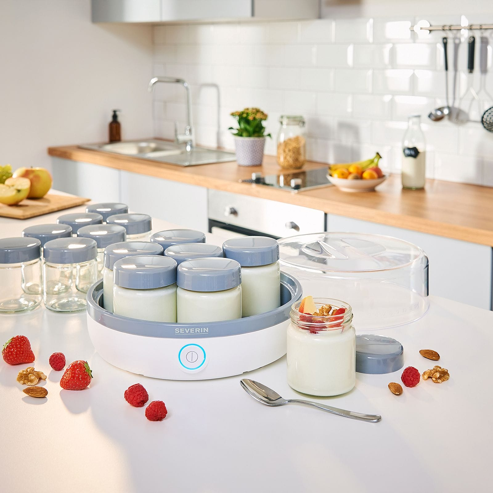 Yogurtera con frascos, fruta y nueces sobre una encimera. Fondo de cocina con fruta, frascos y utensilios.