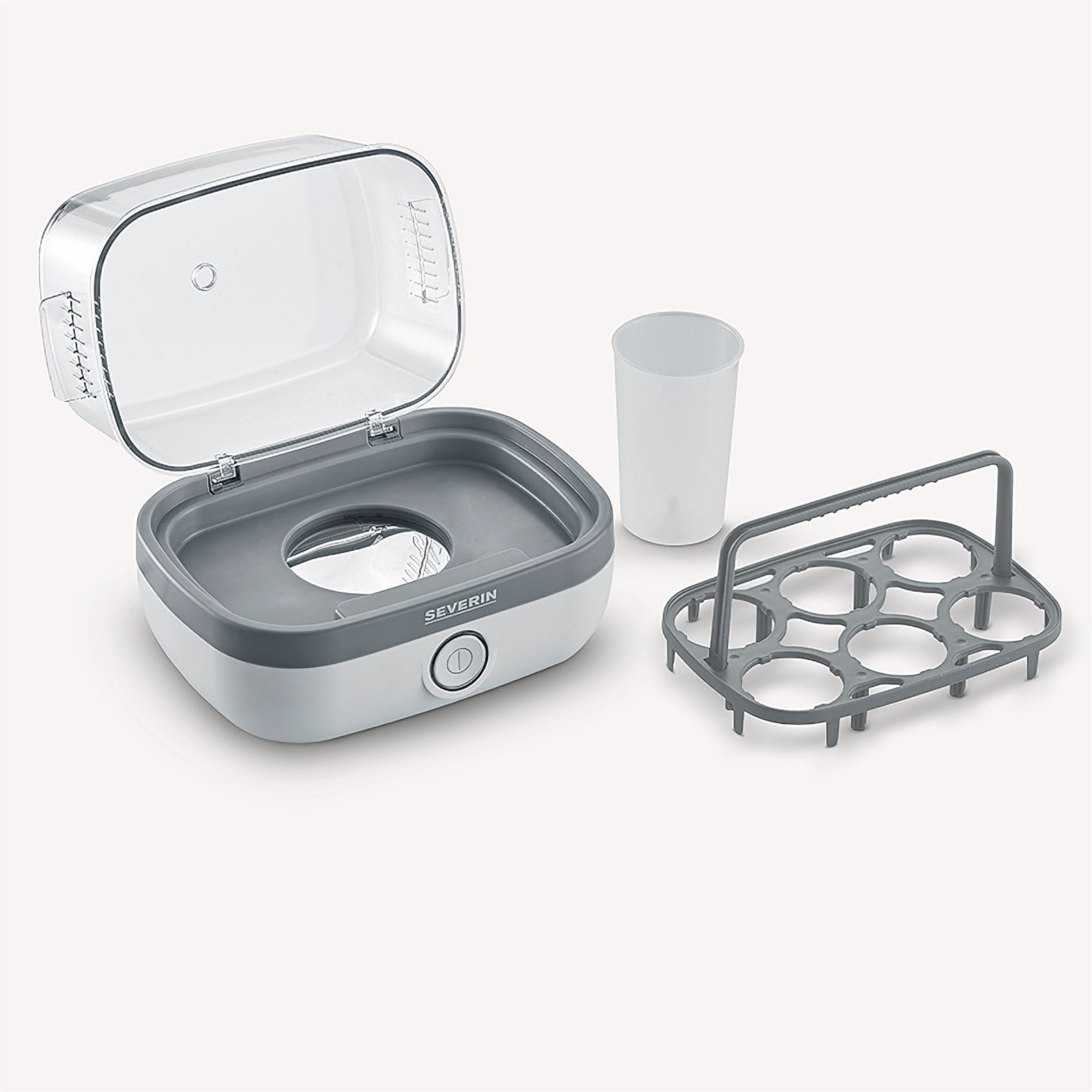 Gotowacz do jajek z akcesoriami. Zawiera gotowacz, kubek na wodę i uchwyt na jajka. Pokrywa jest otwarta.
