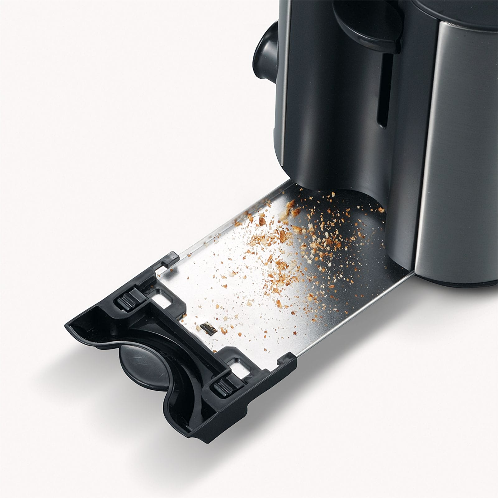 Wysunięta szuflada na okruchy tostera, pokazująca okruchy chleba. Toster jest czarny i srebrny. Białe tło.