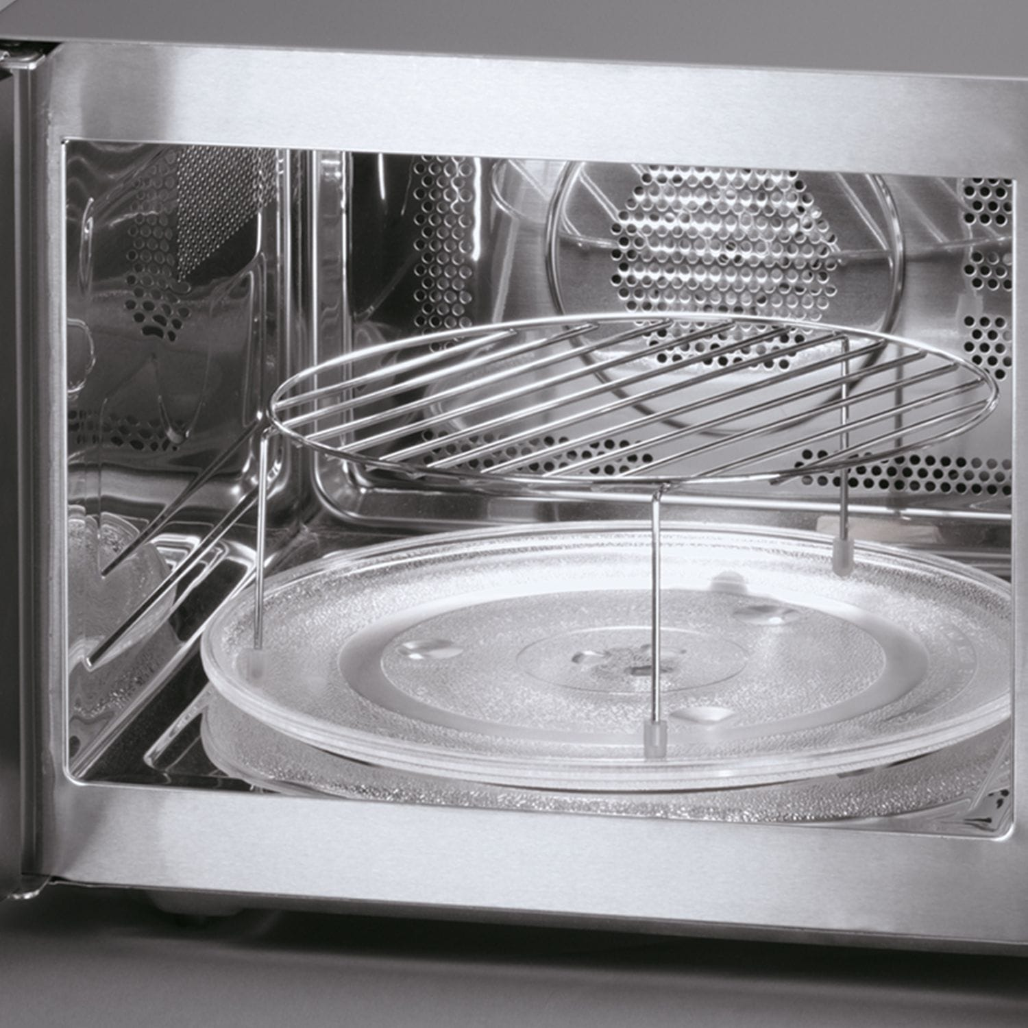 Wnętrze kuchenki mikrofalowej ze stali nierdzewnej. Widoczny szklany talerz obrotowy i druciany ruszt. Wnętrze jest czyste i odbijające światło.