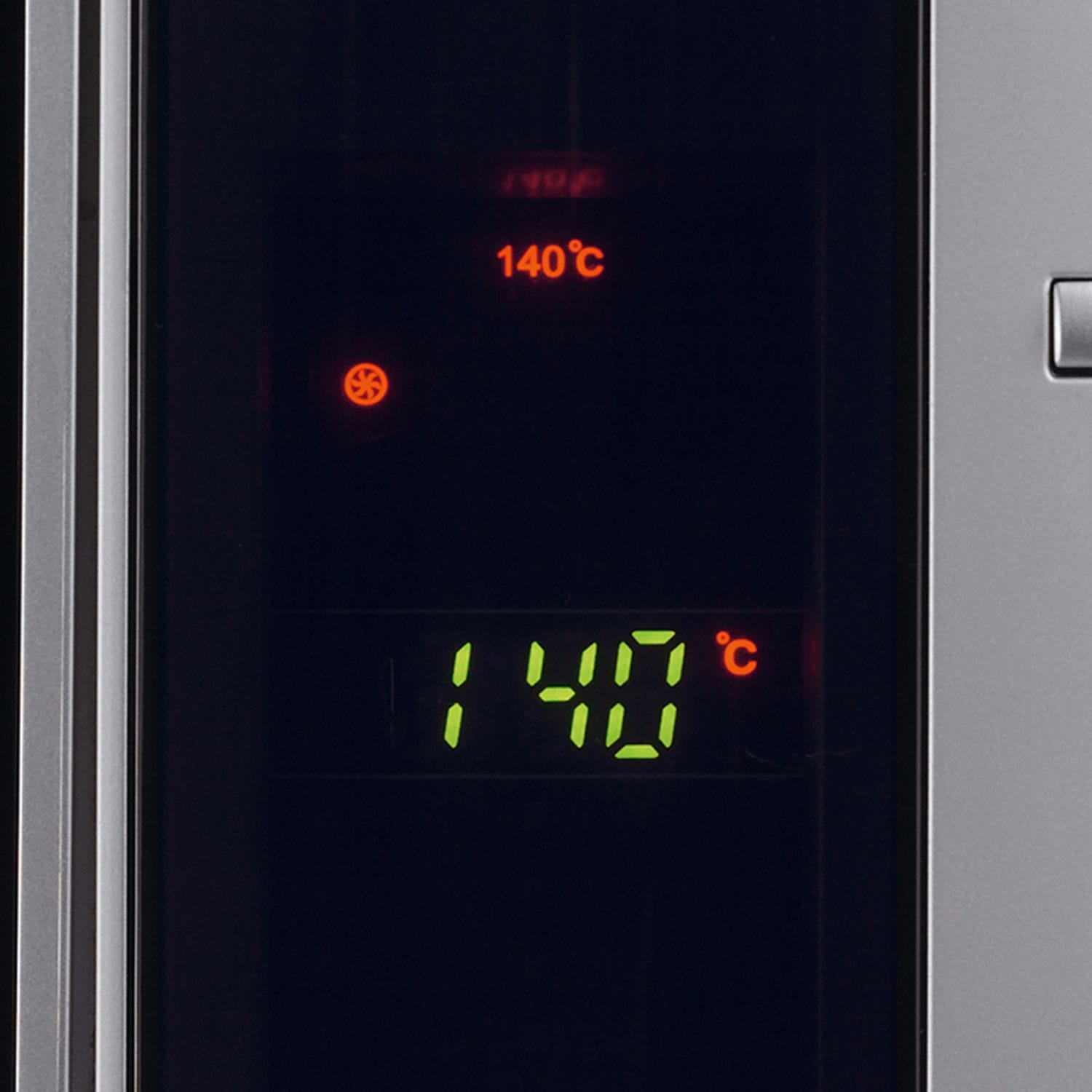 Zbliżenie wyświetlacza kuchenki mikrofalowej pokazującego 140°C w zielonych cyfrach. Powyżej, '140°C' w kolorze pomarańczowym. Obecny jest symbol wentylatora.