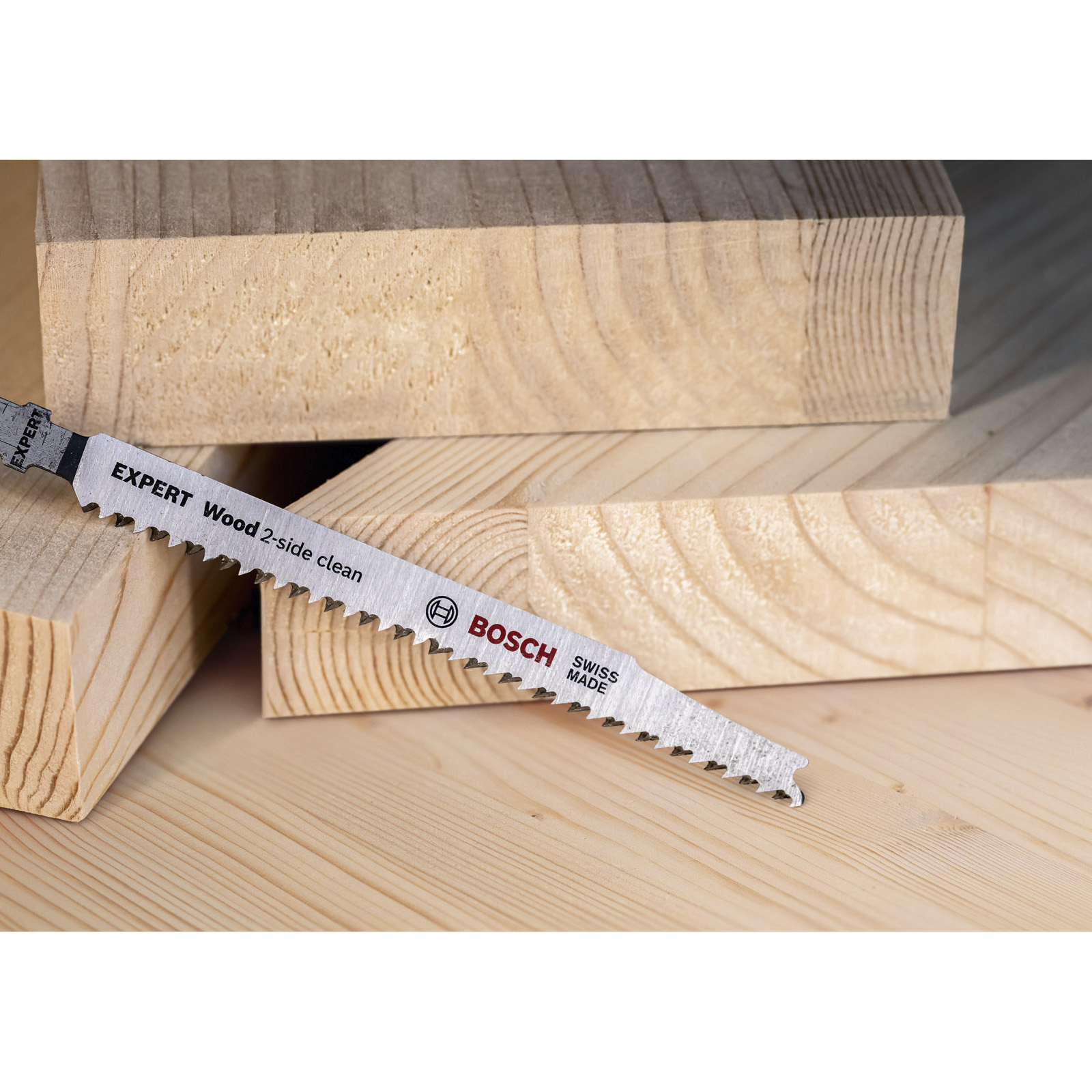 Ostrze piły Bosch leży na drewnianych deskach. Ostrze jest srebrne i ma napis 'EXPERT Wood 2-side clean'.