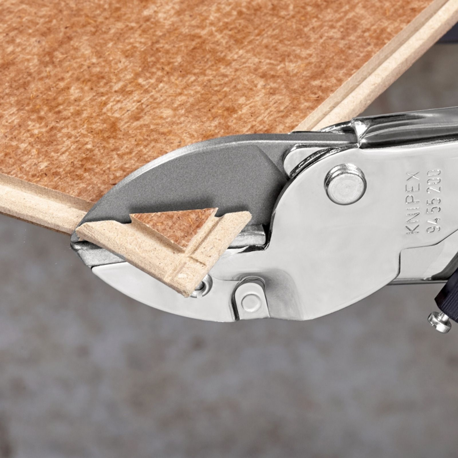 Ein Metallschneider schneidet eine Holzplatte. Das Holz ist hellbraun und der Schneider ist silberfarben. Der Hintergrund ist grau.