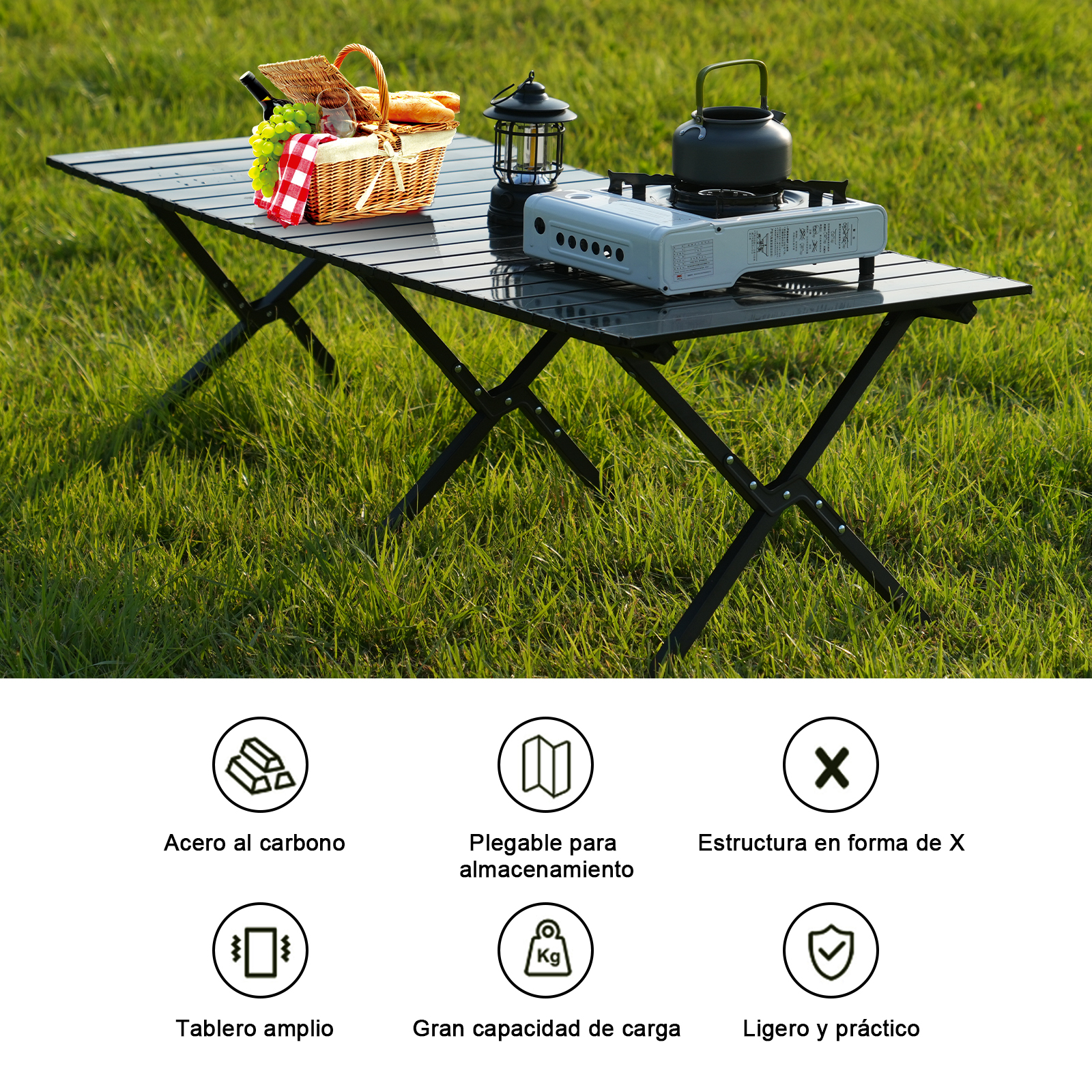 Una mesa plegable negra con elementos de picnic encima, colocada sobre hierba verde. También hay una estufa de camping y una tetera.