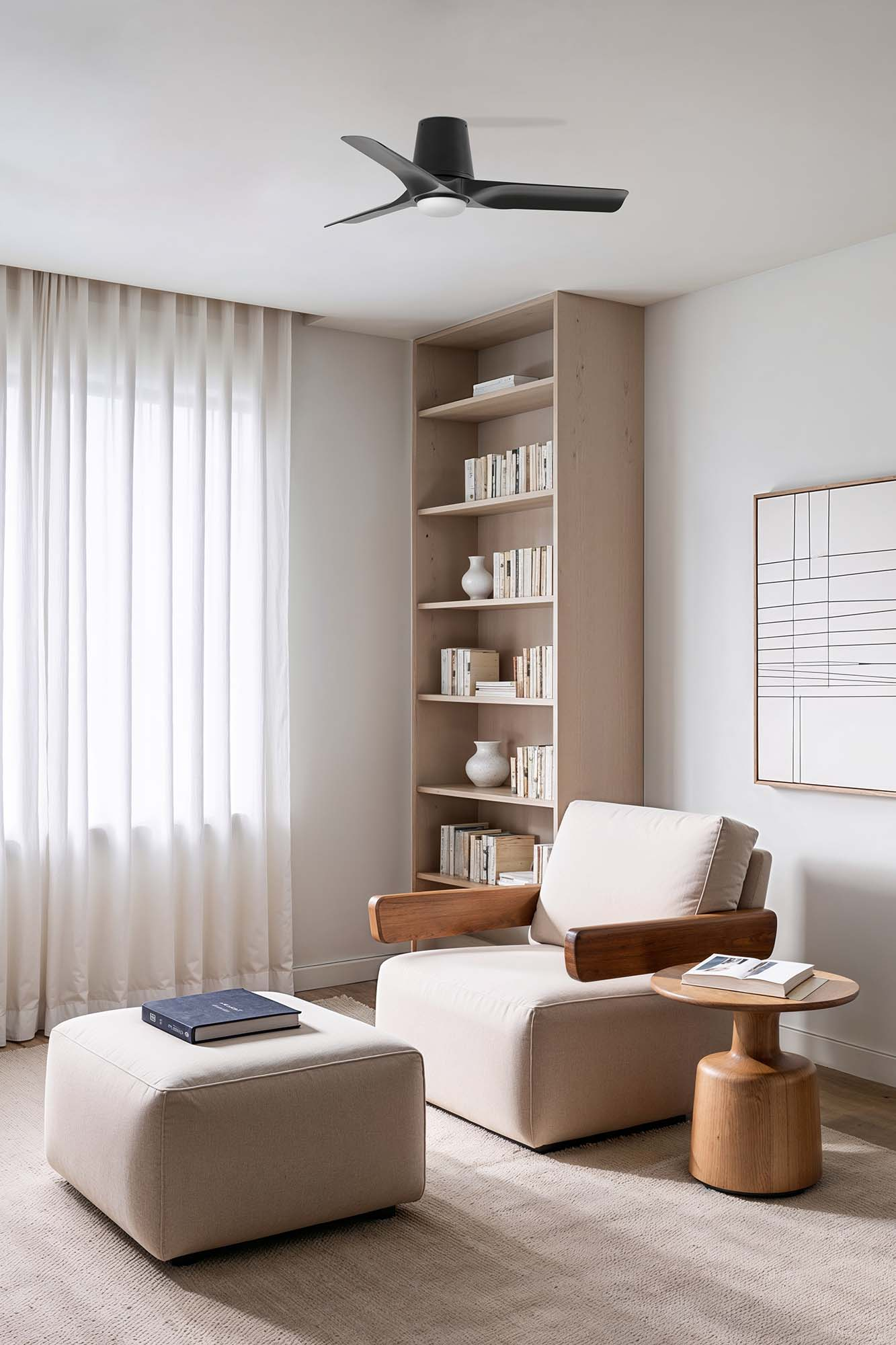 Un soggiorno moderno con ventilatore a soffitto, poltrona, libreria, pouf e tavolino. Luce soffusa e colori neutri.