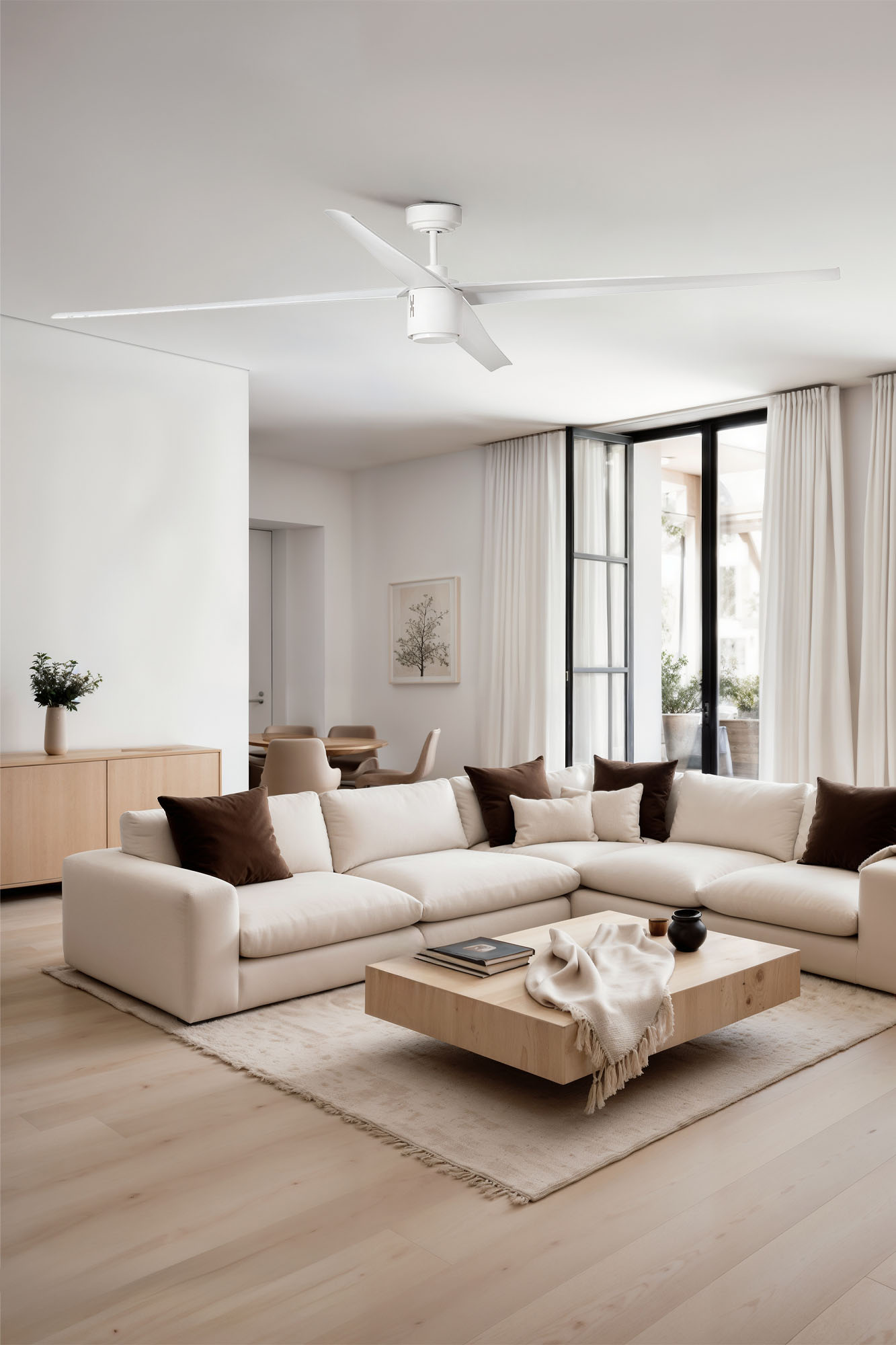 Soggiorno moderno con divano bianco, tavolino in legno e grandi finestre con tende bianche. Un ventilatore a soffitto è appeso.