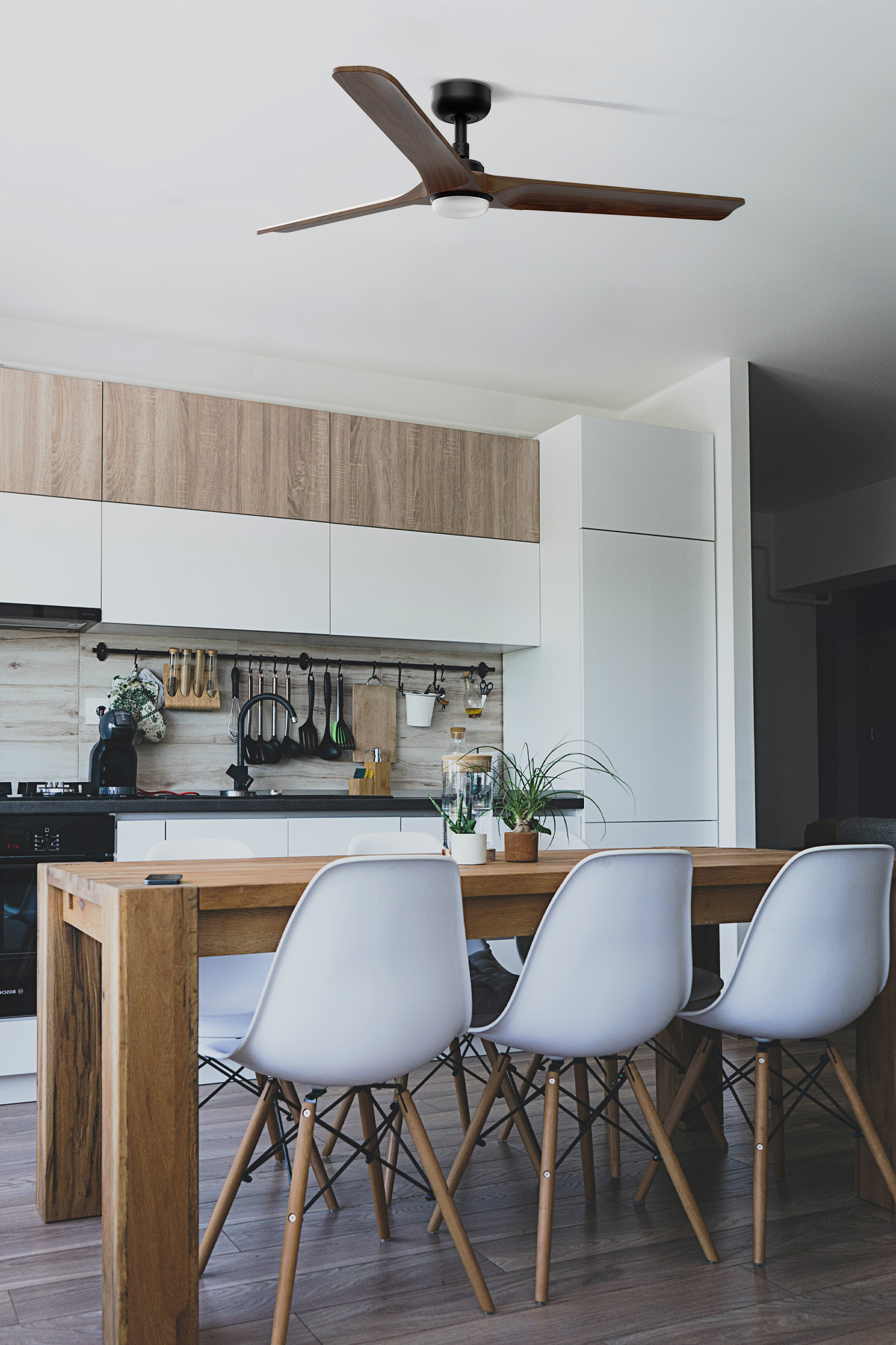 Eine moderne Küche mit Holztisch, weißen Stühlen und Deckenventilator. Schränke haben ein zweifarbiges Design. Pflanzen stehen auf dem Tisch.
