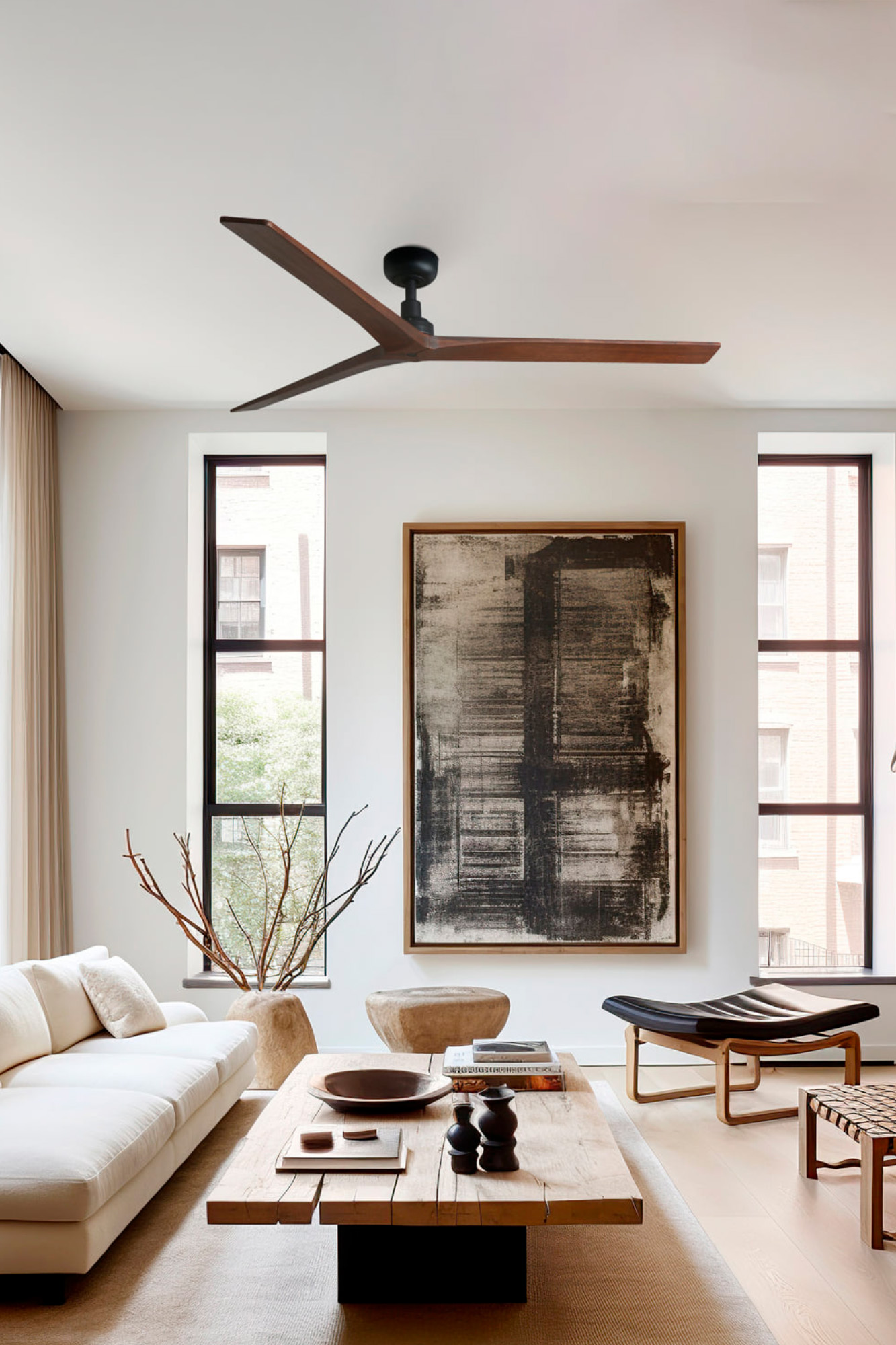 Wohnzimmer mit weißem Sofa, Holztisch, abstrakter Kunst und Deckenventilator. Fenster bieten einen Blick nach draußen.