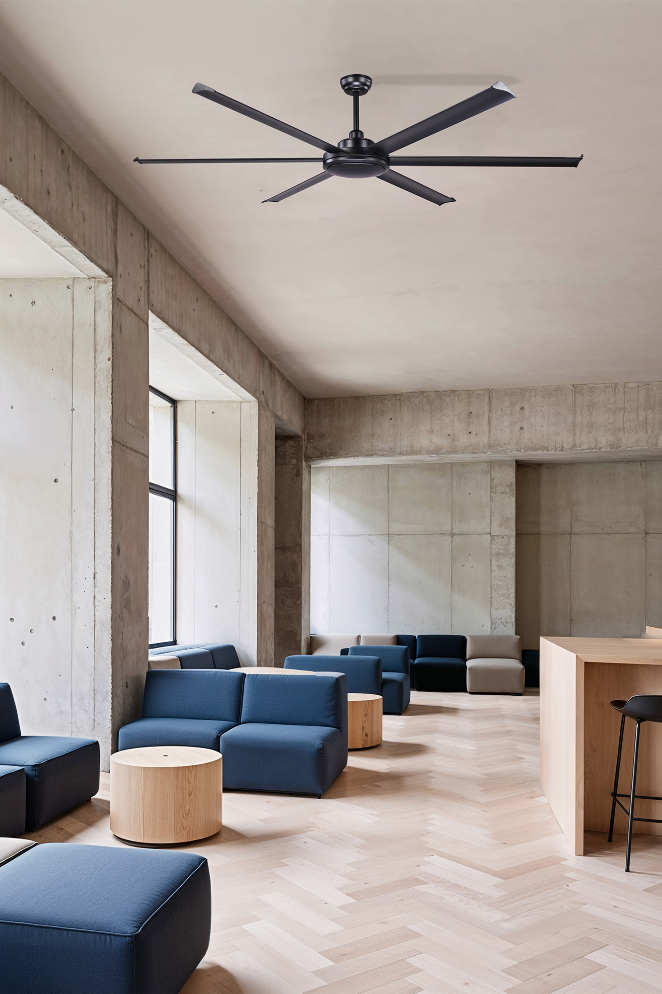 Interni moderni con pareti in cemento, divani blu, tavoli in legno e un grande ventilatore a soffitto nero.