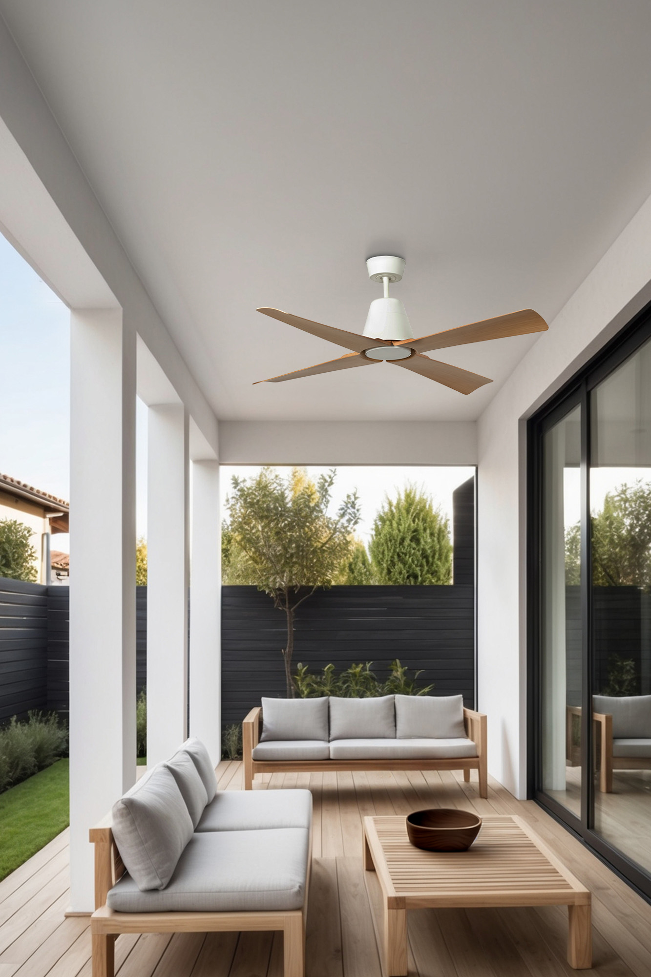 Terrasse im Freien mit grauen Sofas, Holztisch und Deckenventilator. Hintergrund mit Bäumen und schwarzem Zaun.