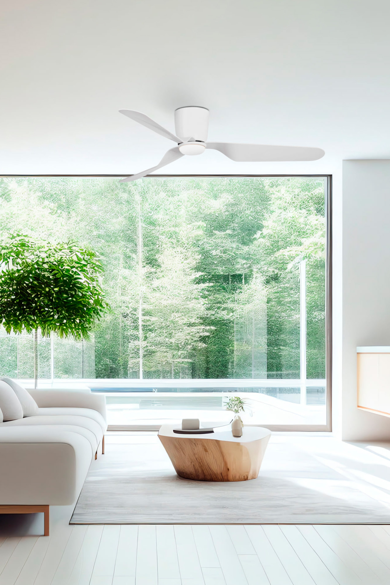 Modernes Wohnzimmer mit weißen Möbeln, einem Holztisch und einem Deckenventilator. Große Fenster bieten einen Blick auf üppig grüne Bäume.