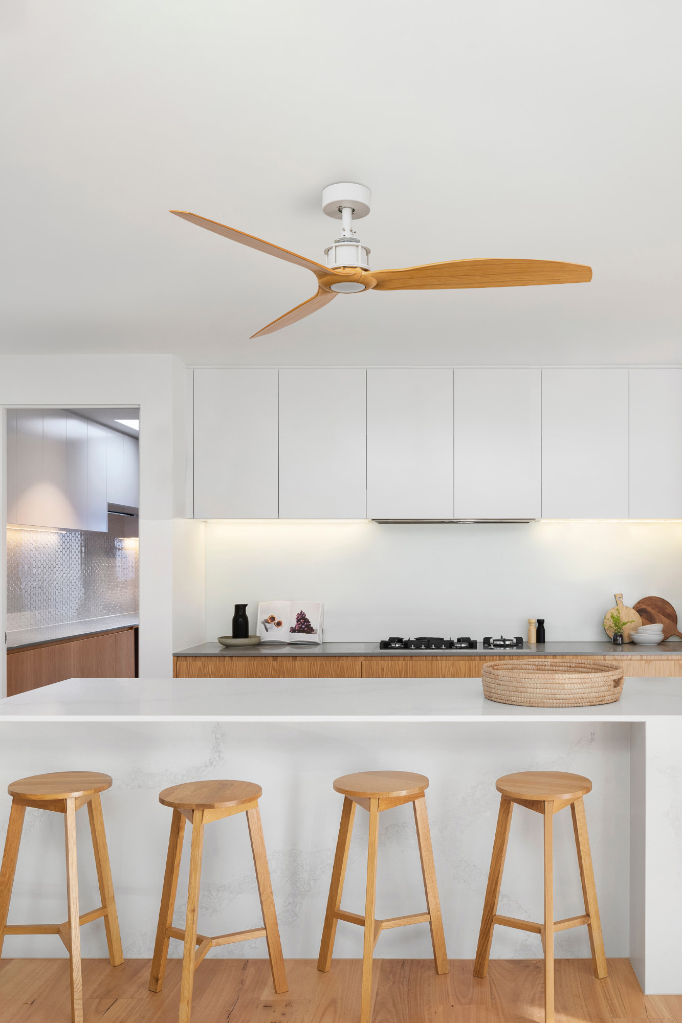 Eine moderne Küche mit Deckenventilator, weißen Schränken, Hockern und einer Arbeitsplatte. Ein geflochtener Korb liegt auf der Theke.