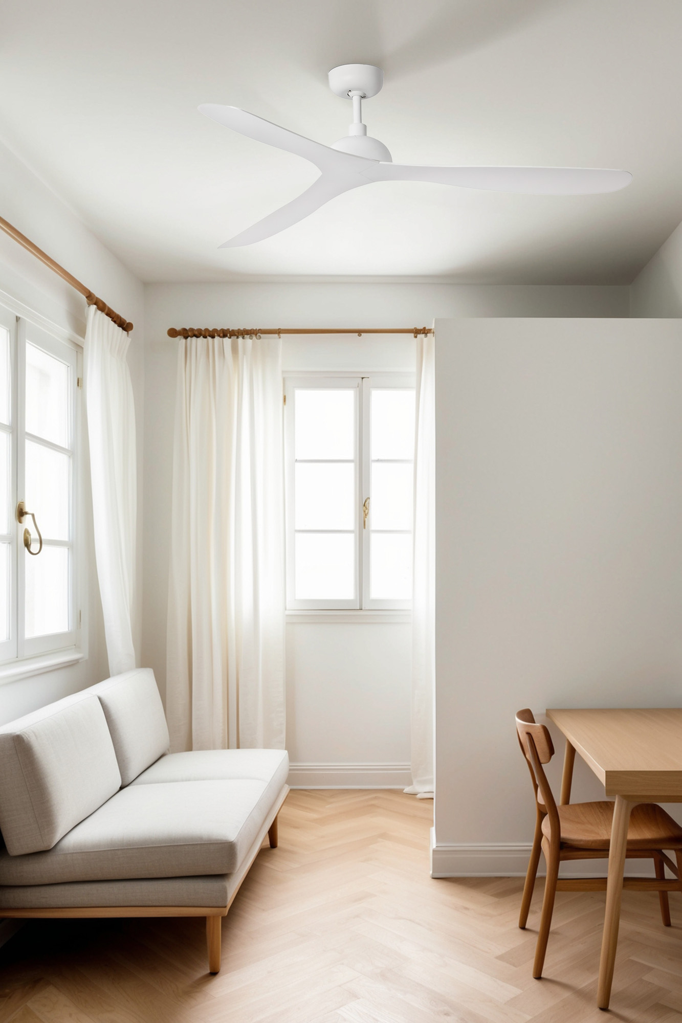 Una stanza luminosa con ventilatore a soffitto, finestre, tende bianche, divano, tavolo e sedia. Pavimento in legno.