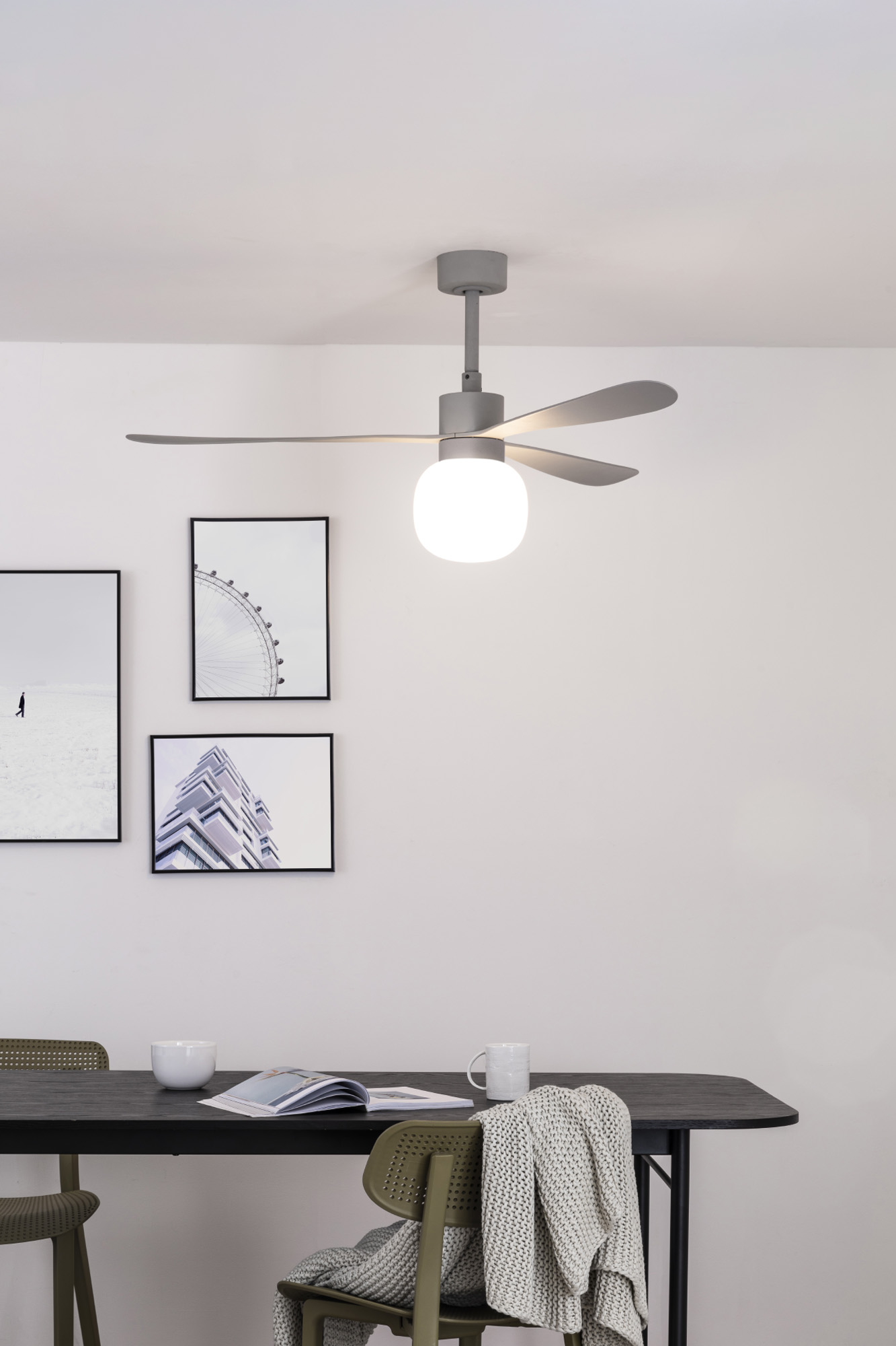 Ein modernes Esszimmer mit Deckenventilator und Kunst. Ein Tisch hat Stühle, Tassen und eine Decke. Der Raum ist hell.