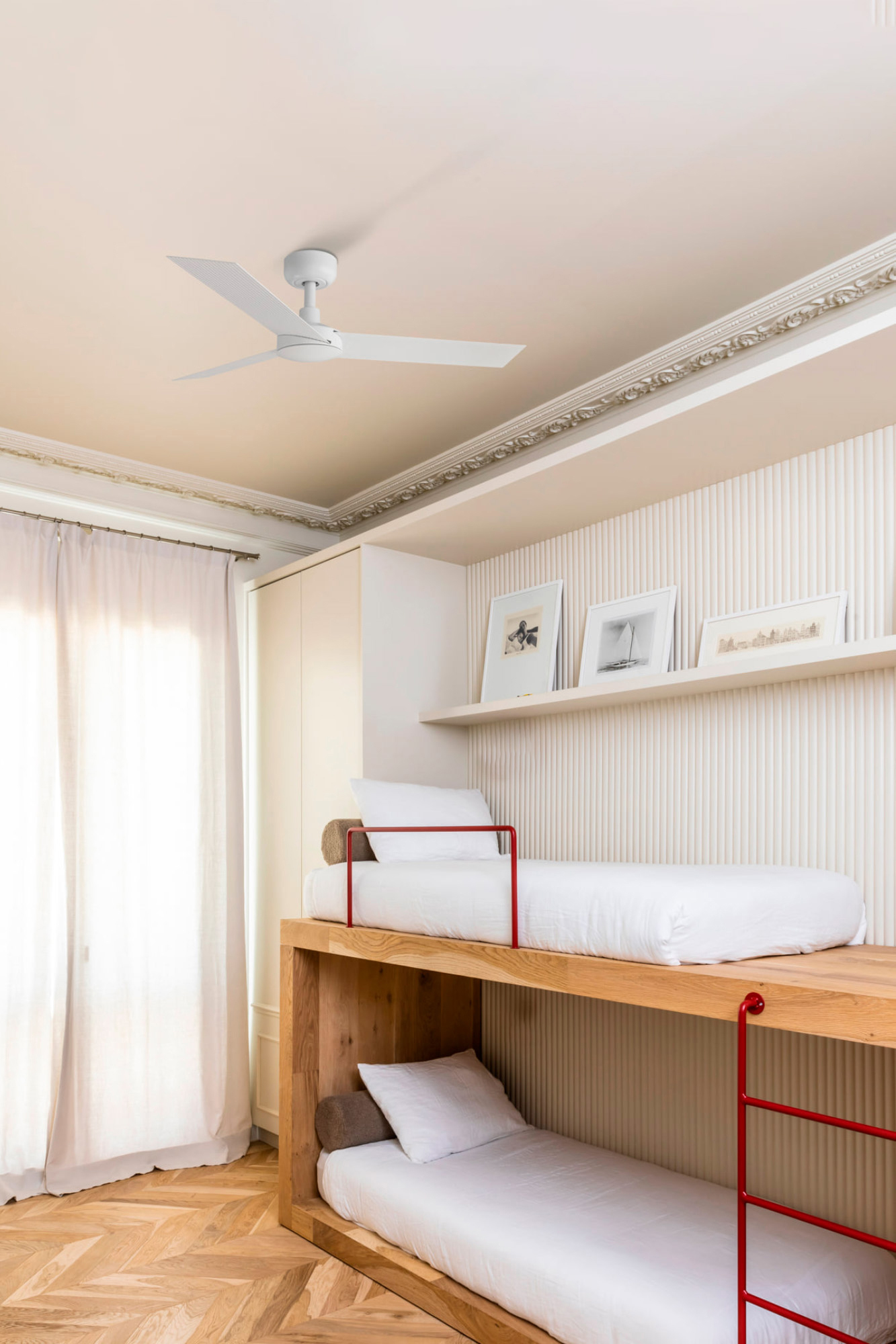 Schlafzimmer mit Etagenbetten. Die Betten haben weiße Bettwäsche und rote Geländer. Der Raum hat Holzböden und einen Deckenventilator.