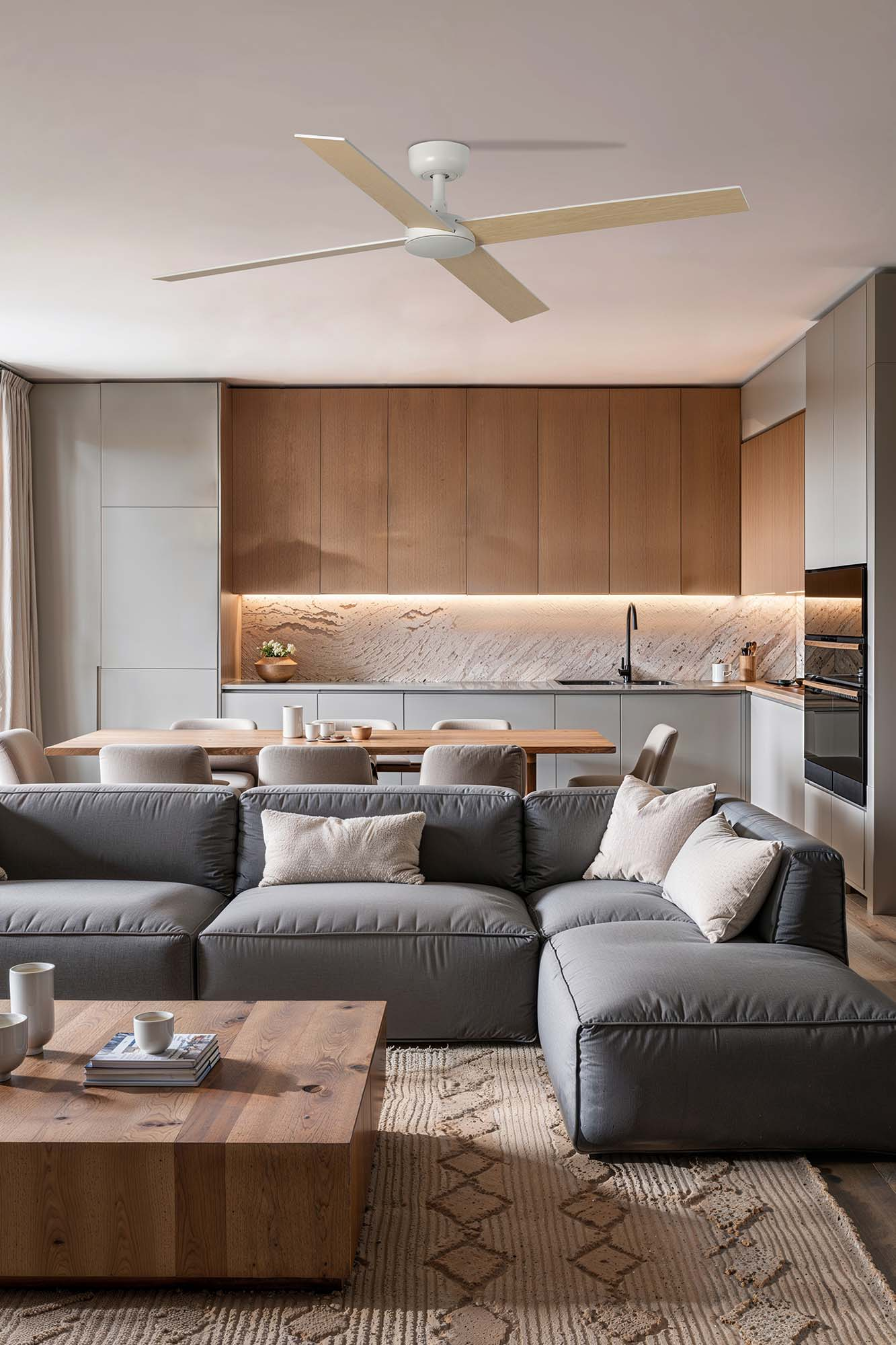 Modernes Wohnzimmer mit grauem Ecksofa, Holztisch und Deckenventilator. Küche im Hintergrund.