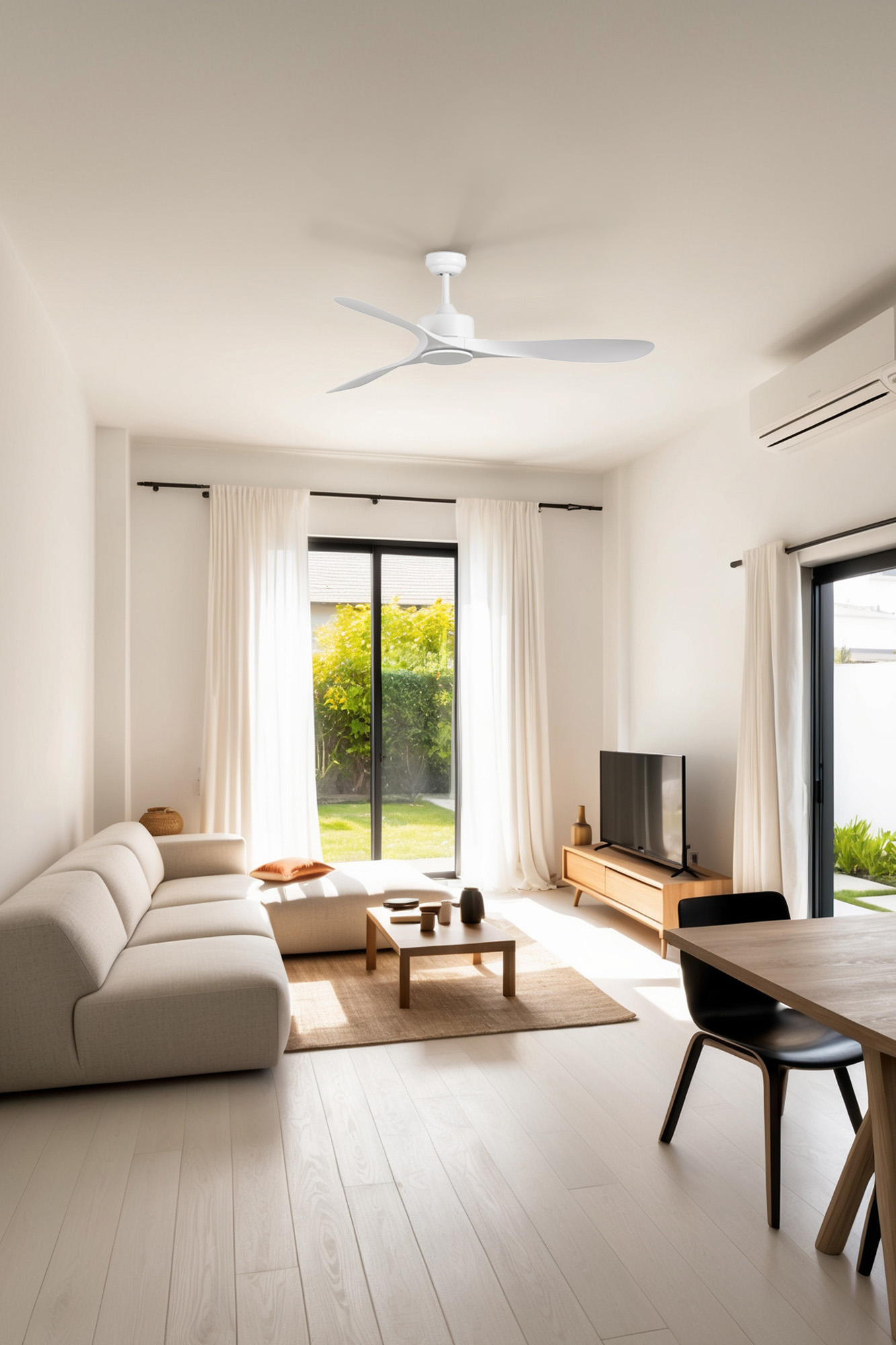 Modernes Wohnzimmer mit weißen Wänden, Sofa, Fernseher und Deckenventilator. Große Fenster blicken auf einen grünen Garten.