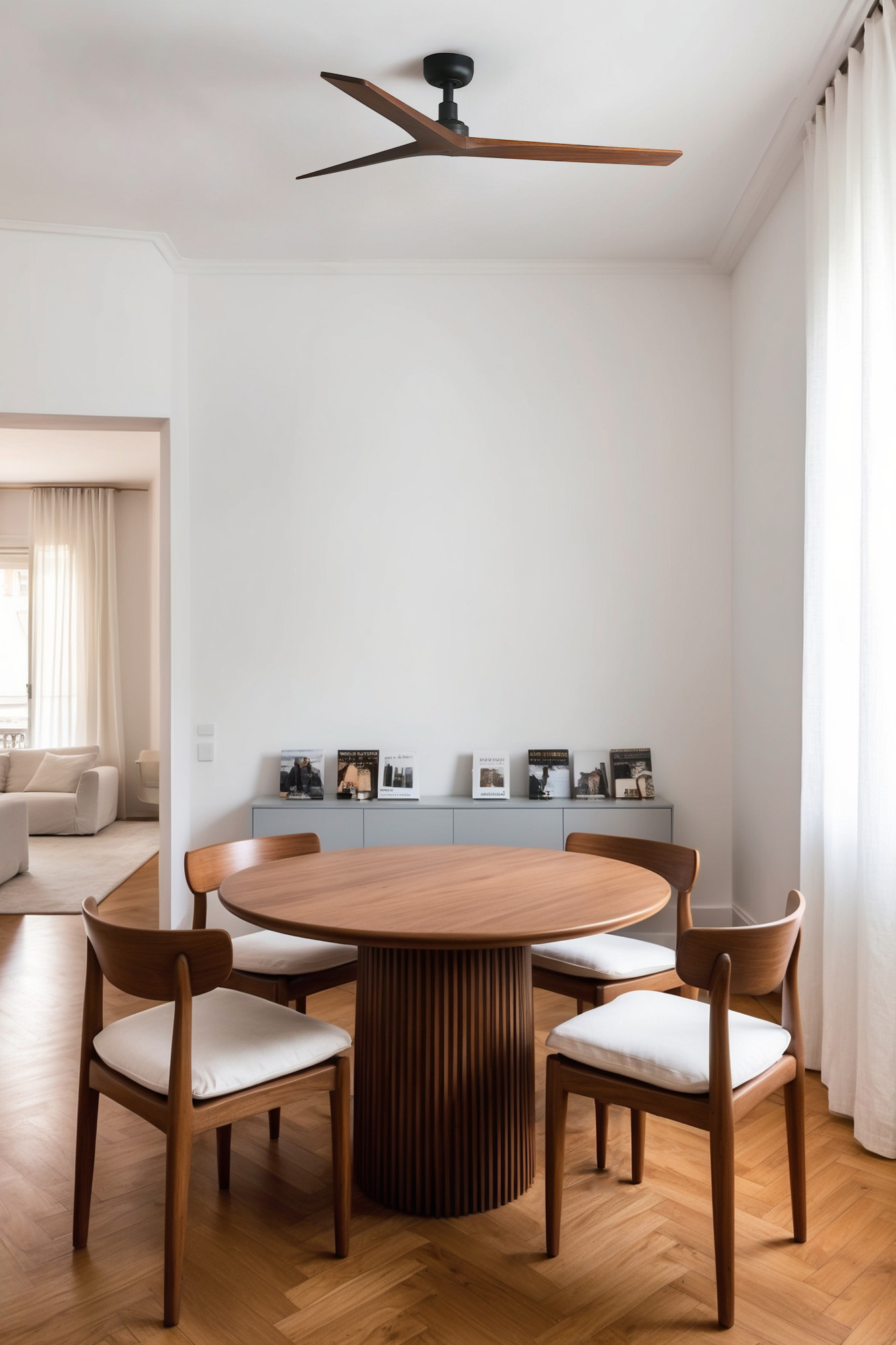 Innenaufnahme eines Essbereichs. Ein Holztisch mit vier Stühlen, Deckenventilator, Bücher auf einem Regal und ein Fenster mit transparenten Vorhängen.