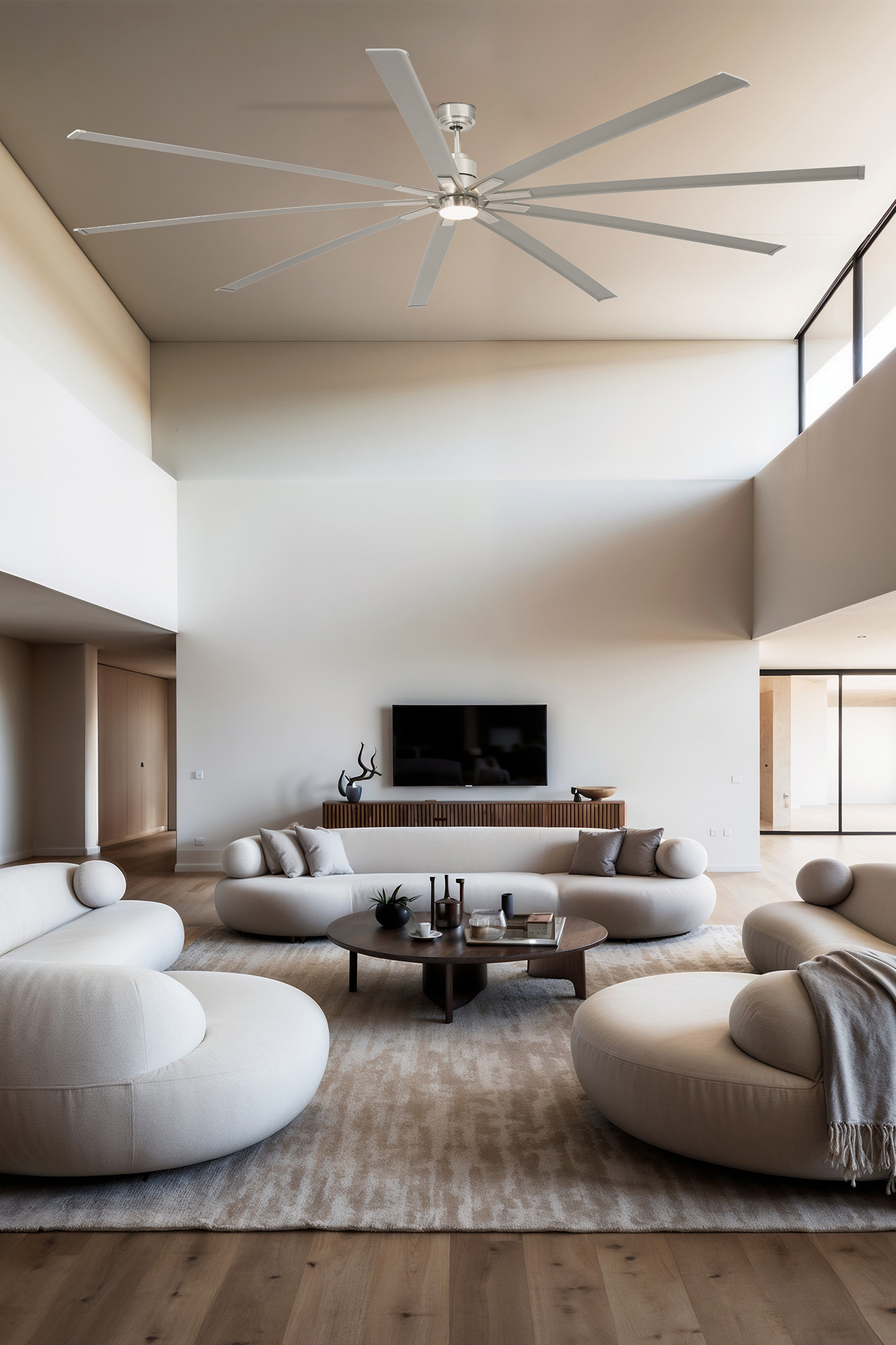 Modernes Wohnzimmer mit weißen Sofas, Holzboden, großem Deckenventilator, Fernseher und rundem Couchtisch auf einem Teppich.