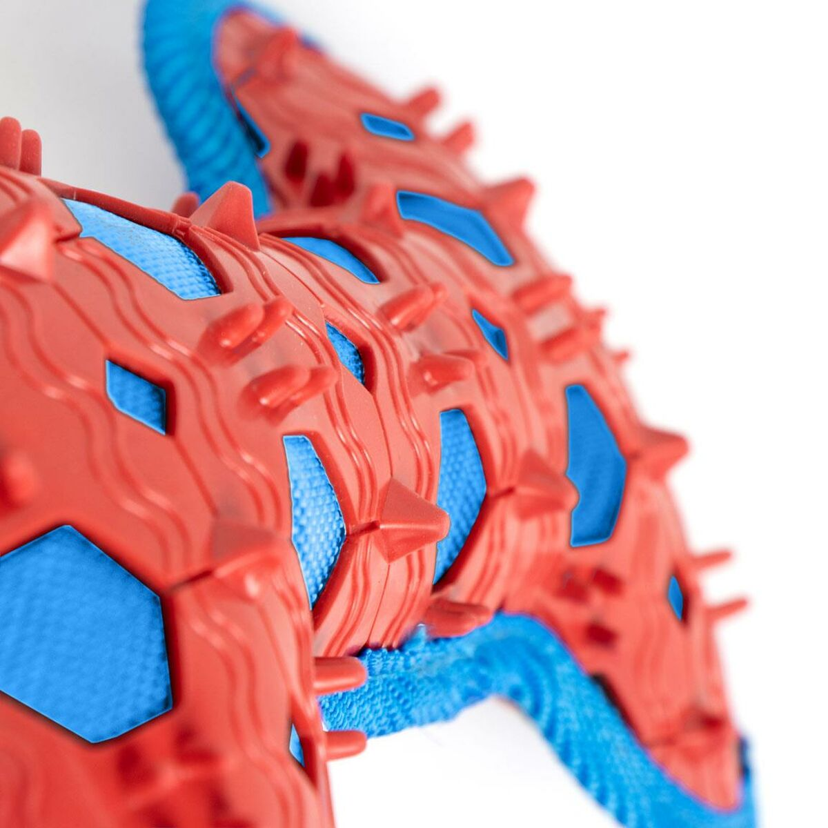 Primo piano di un giocattolo per cani strutturato rosso e blu. Ha punte e motivi geometrici, con sfondo bianco.