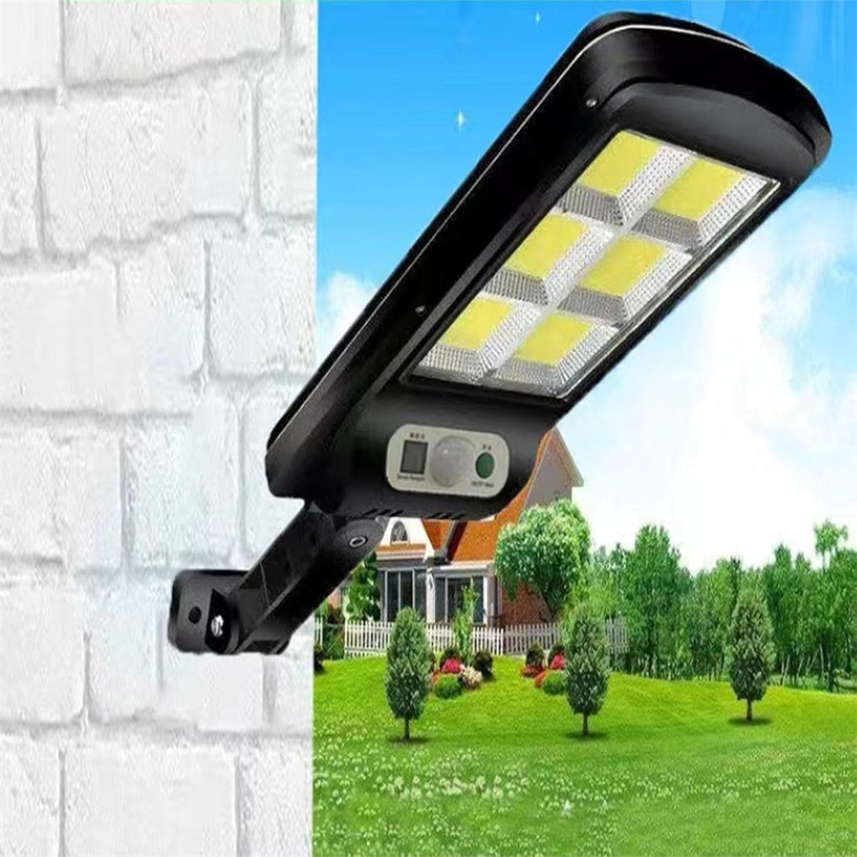 Schwarze Solarlampe an einer weißen Ziegelmauer befestigt. Im Hintergrund sind Haus, Bäume und grünes Gras unter blauem Himmel.