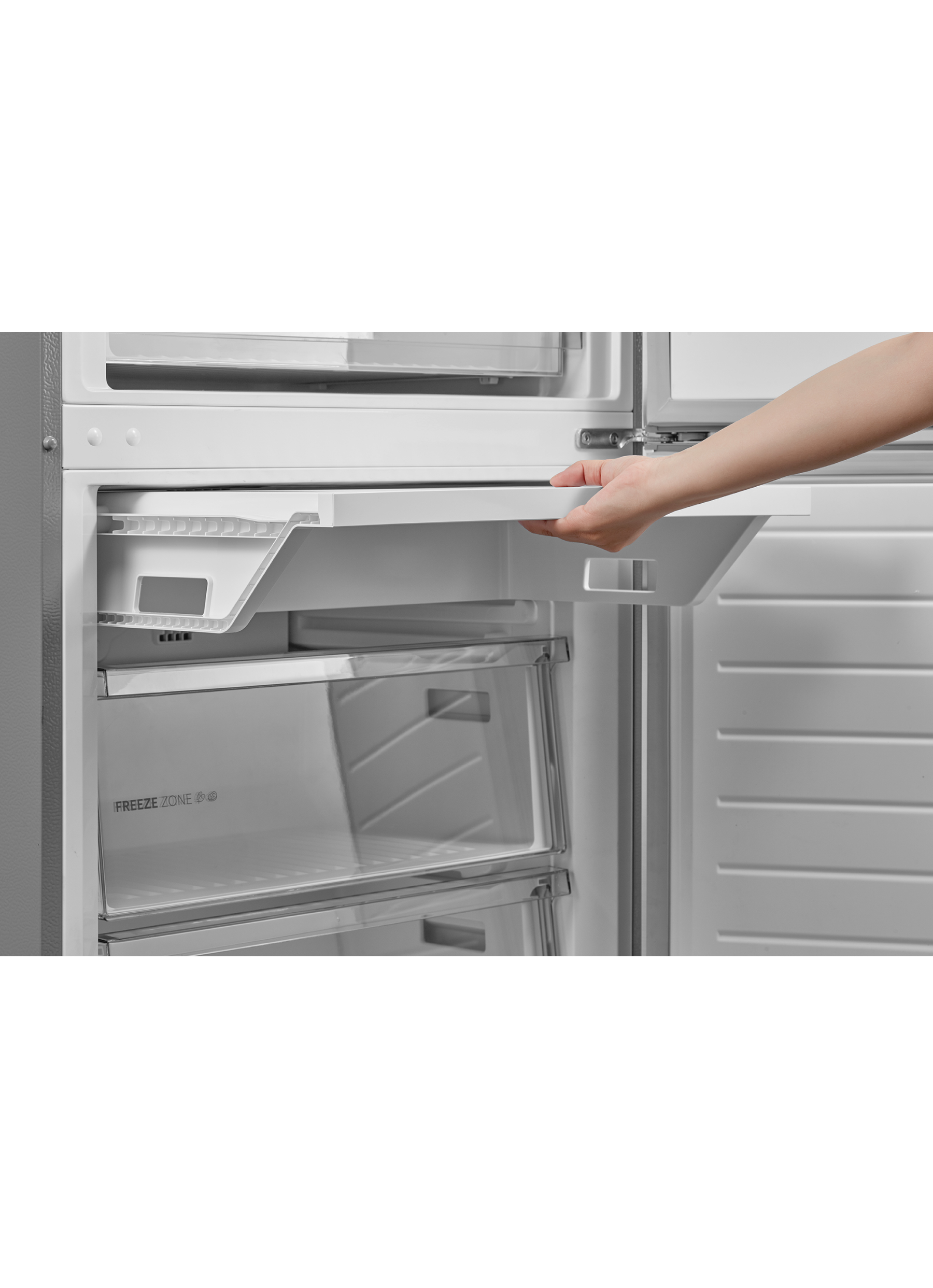 Una mano estrae un ripiano bianco del frigorifero. Il cassetto del congelatore è visibile. Il frigo è aperto.